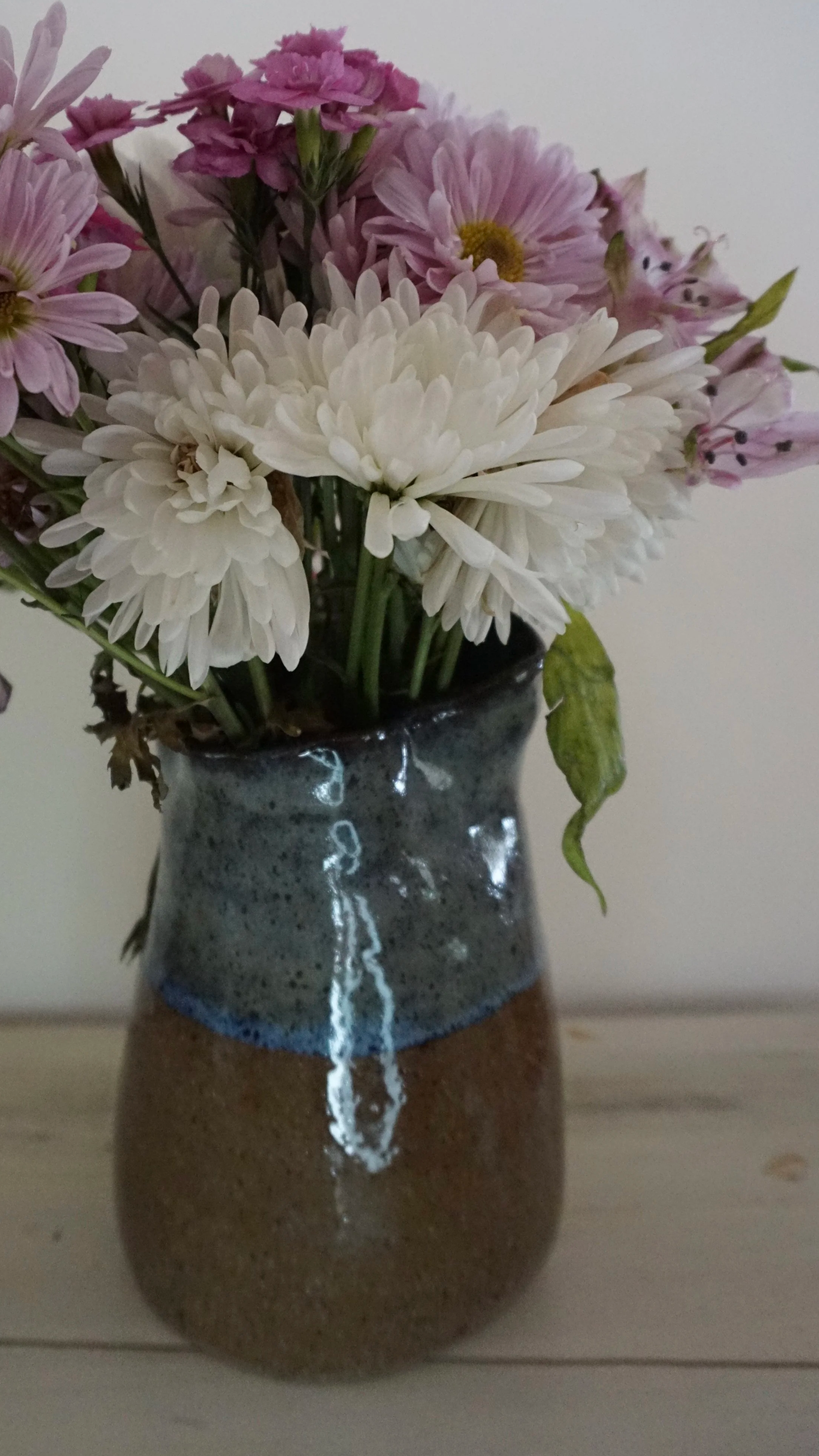 A ceramic vase holding a bouquet of purple, pink, and white flowers, placed on a wooden surface.