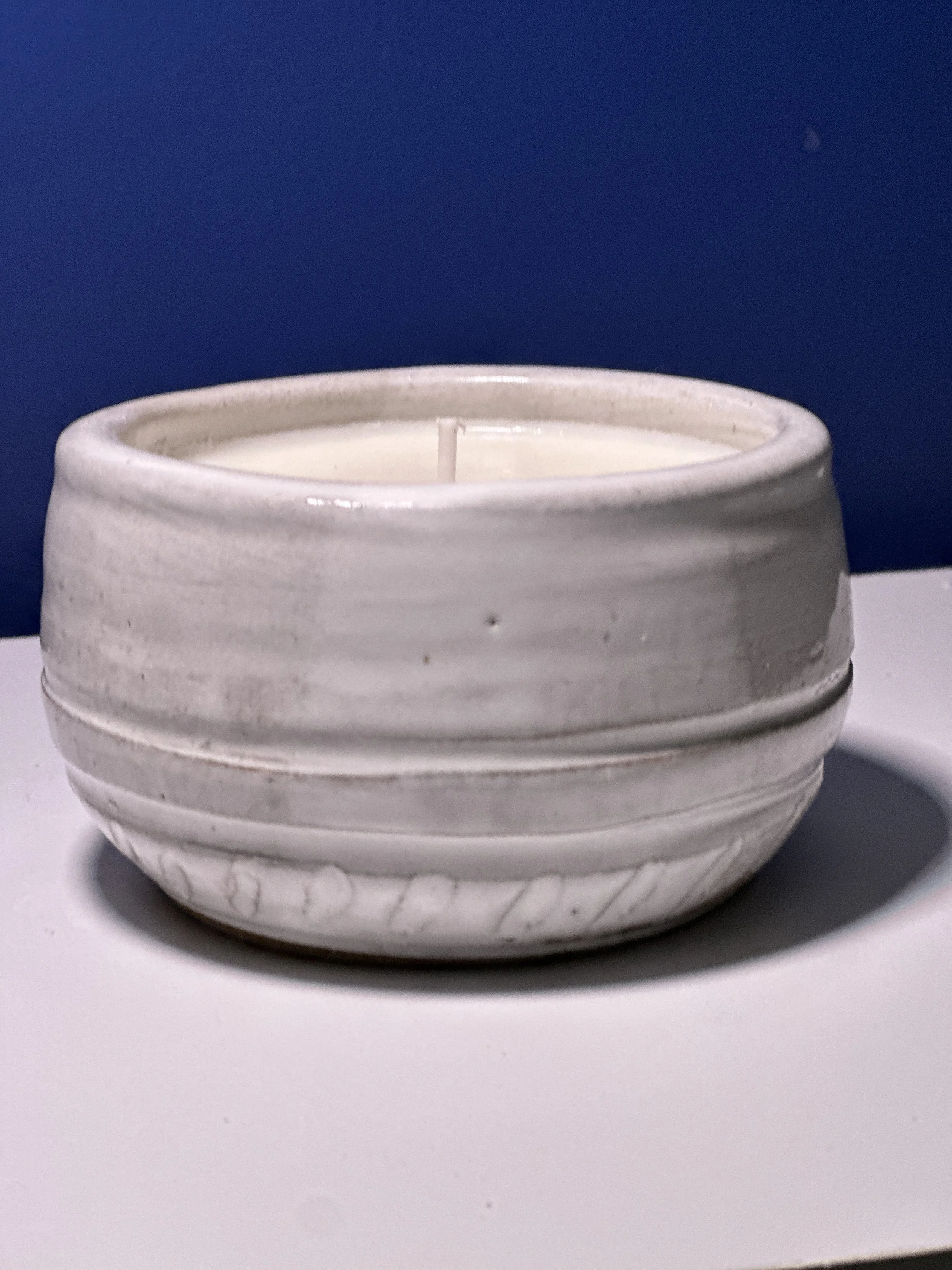 White ceramic bowl with a candle inside, placed on a white surface against a blue wall.