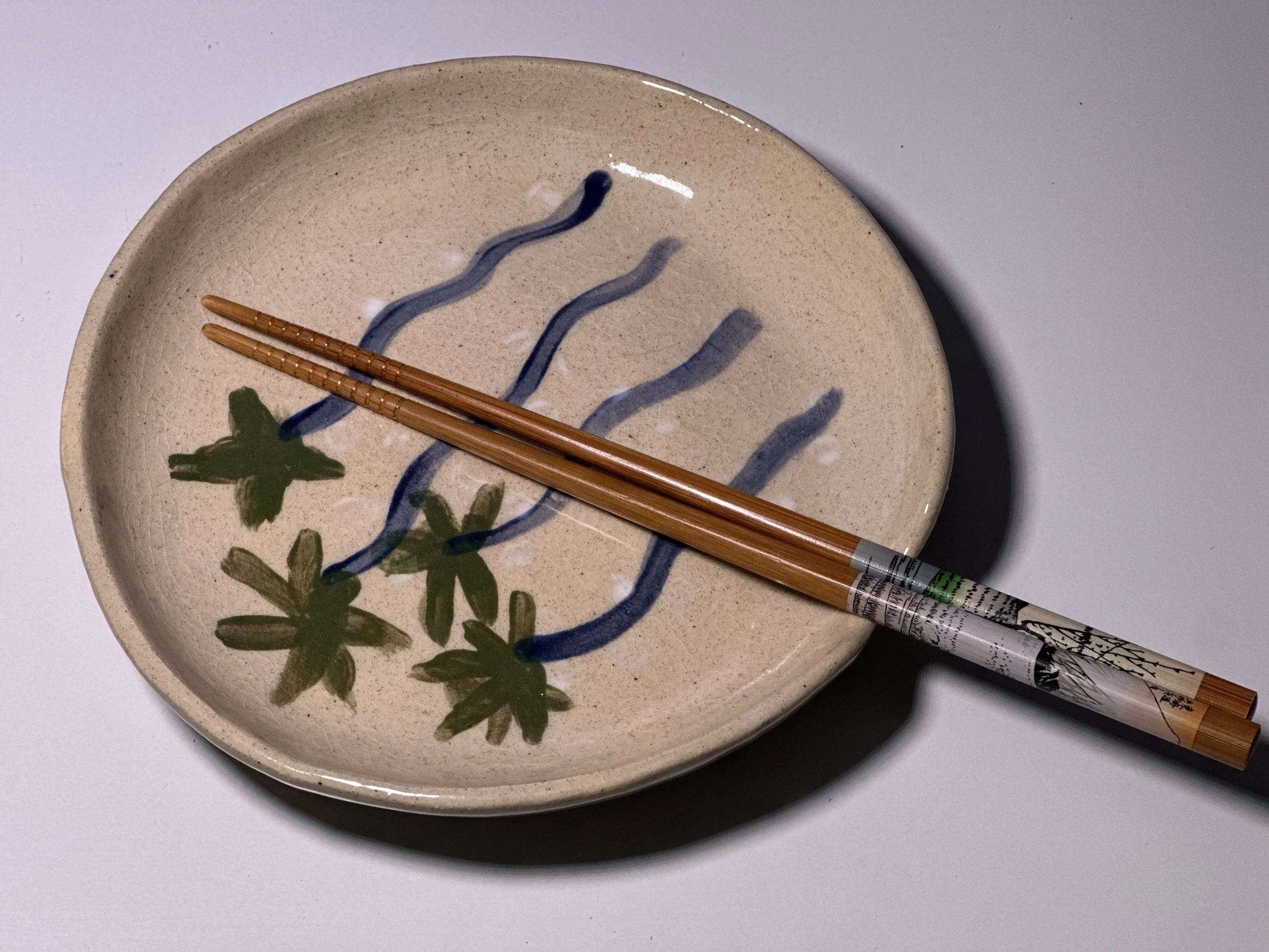 A ceramic plate with a floral design, placed on a white surface with a pair of wooden chopsticks resting on it.