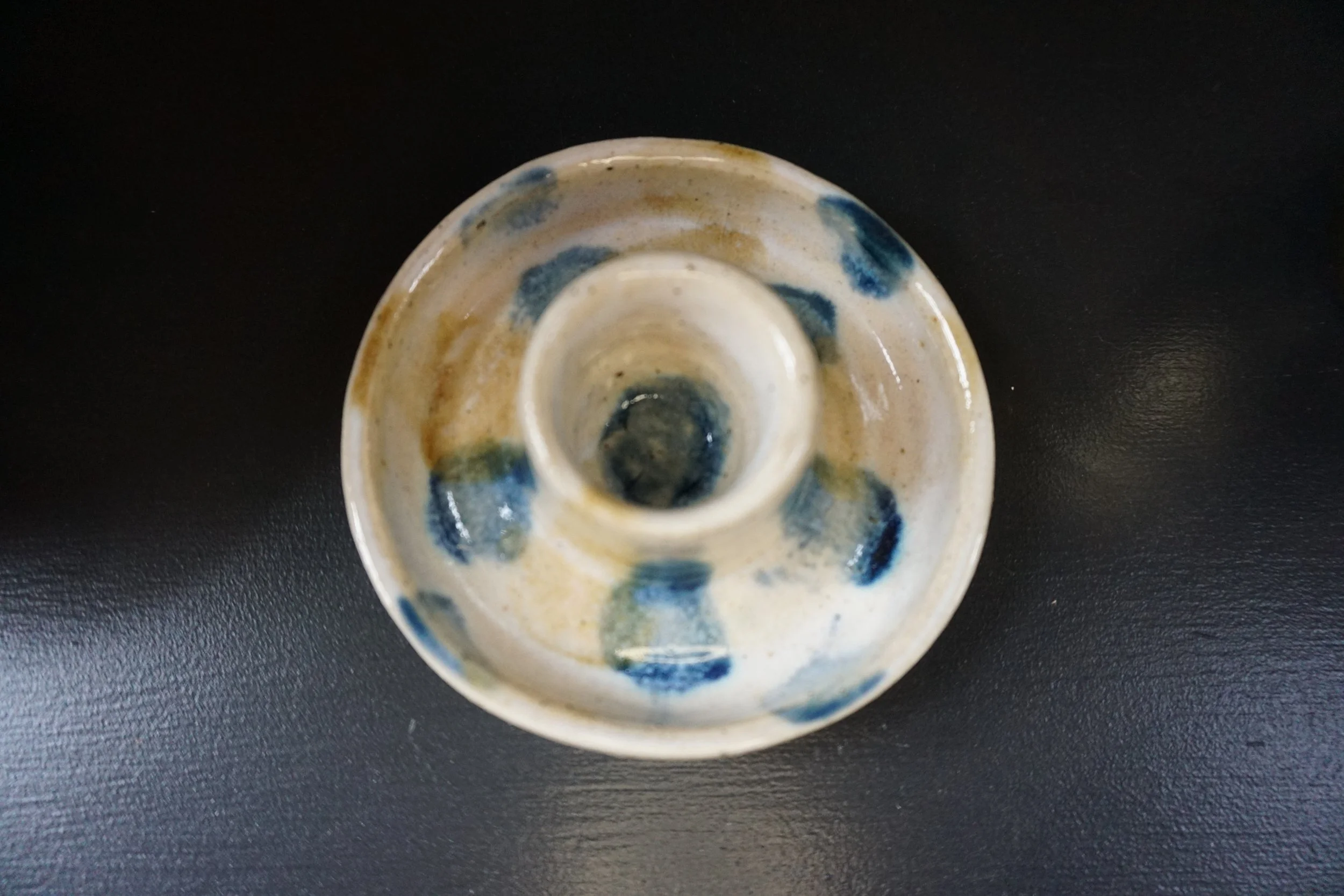 Top view of a small ceramic object with blue and beige glaze, placed on a black surface.