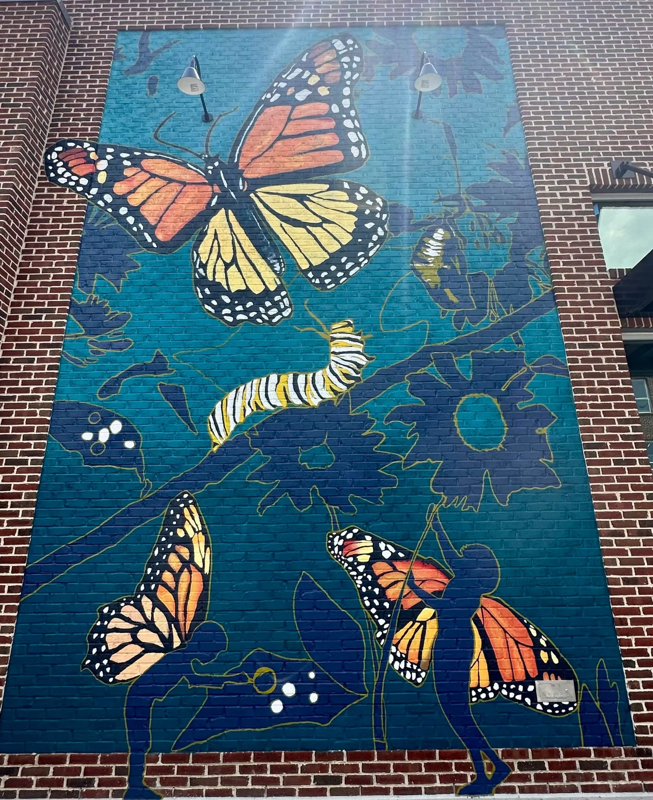 Colorful mural of butterflies, caterpillars, and flowers on a brick wall.