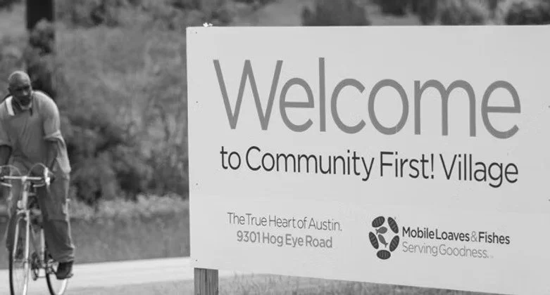 A man riding a bicycle next to a sign that says, 'Welcome to Community First! Village' in Austin, Texas.