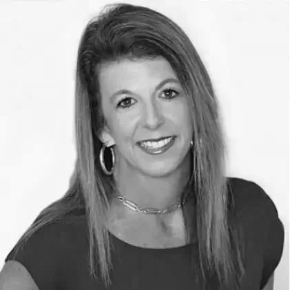 A woman with long, straight hair, wearing hoop earrings and a necklace, smiling at the camera.