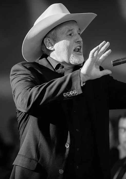 A man wearing a cowboy hat and a suit is speaking passionately, gesturing with one hand, in a black and white photograph.
