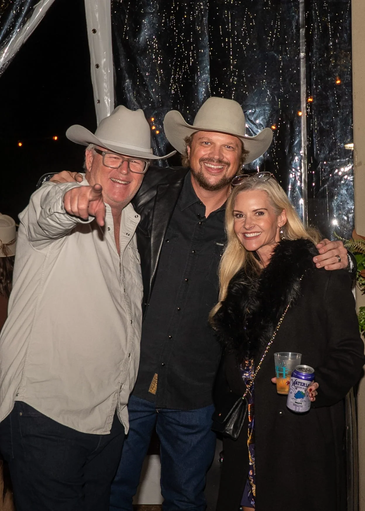 Three people wearing cowboy hats at a festive event, standing close together and smiling for the camera.