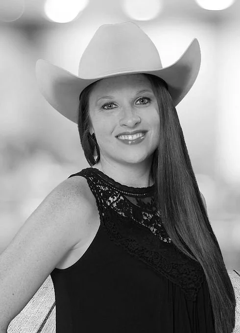 Woman wearing a cowboy hat and a lace black top, smiling, with long straight hair.