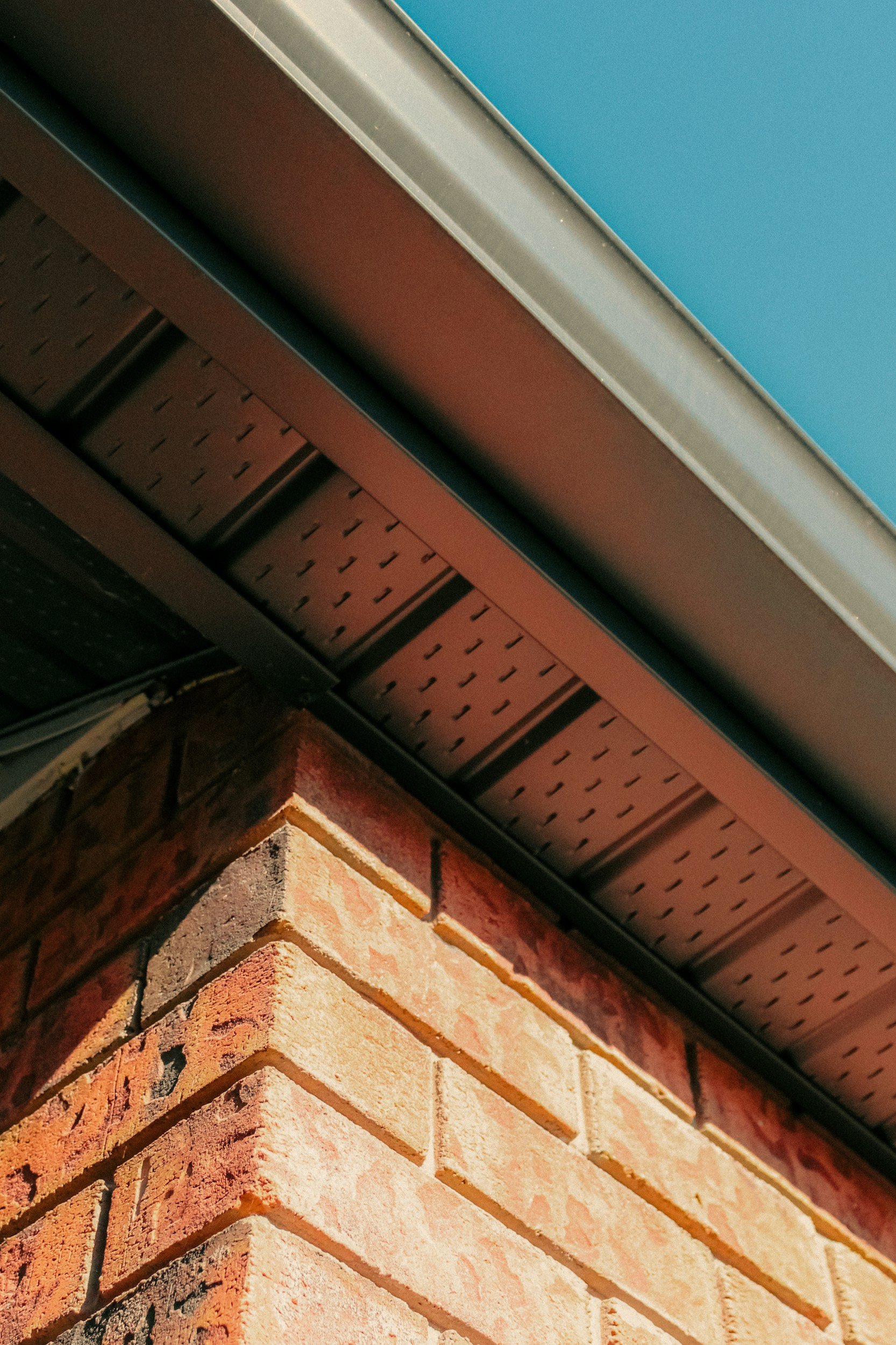 Close-up of brick wall corner with a metal ventilation duct and a blue ceiling.