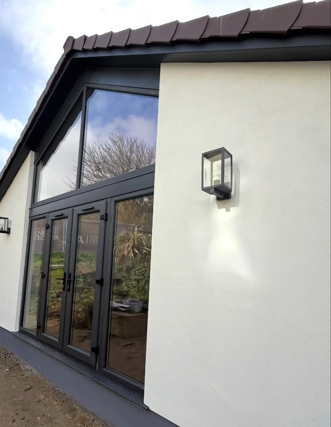 Exterior view of a modern house with white walls, black window frames, and a black front door, with an outdoor wall-mounted light fixture