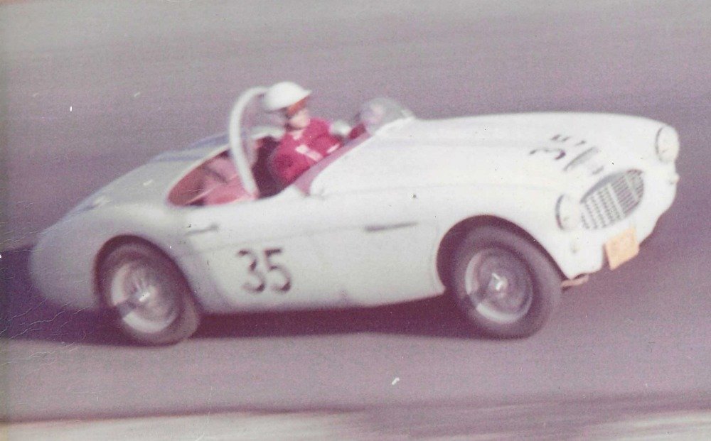 Vintage race car with the number 35 driven by a person in a pink suit and white helmet.