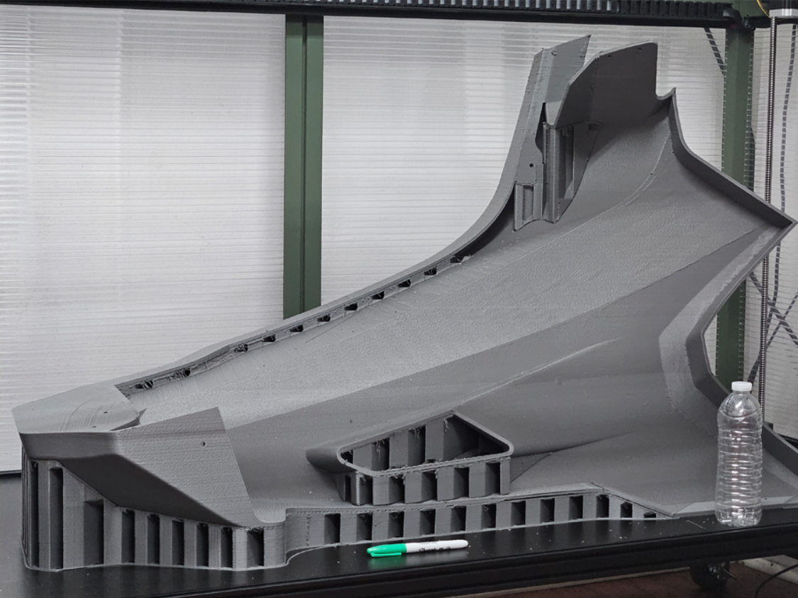 Full-scale 3D printed automotive fender prototype. A marker and water bottle are placed next to the part for size reference.