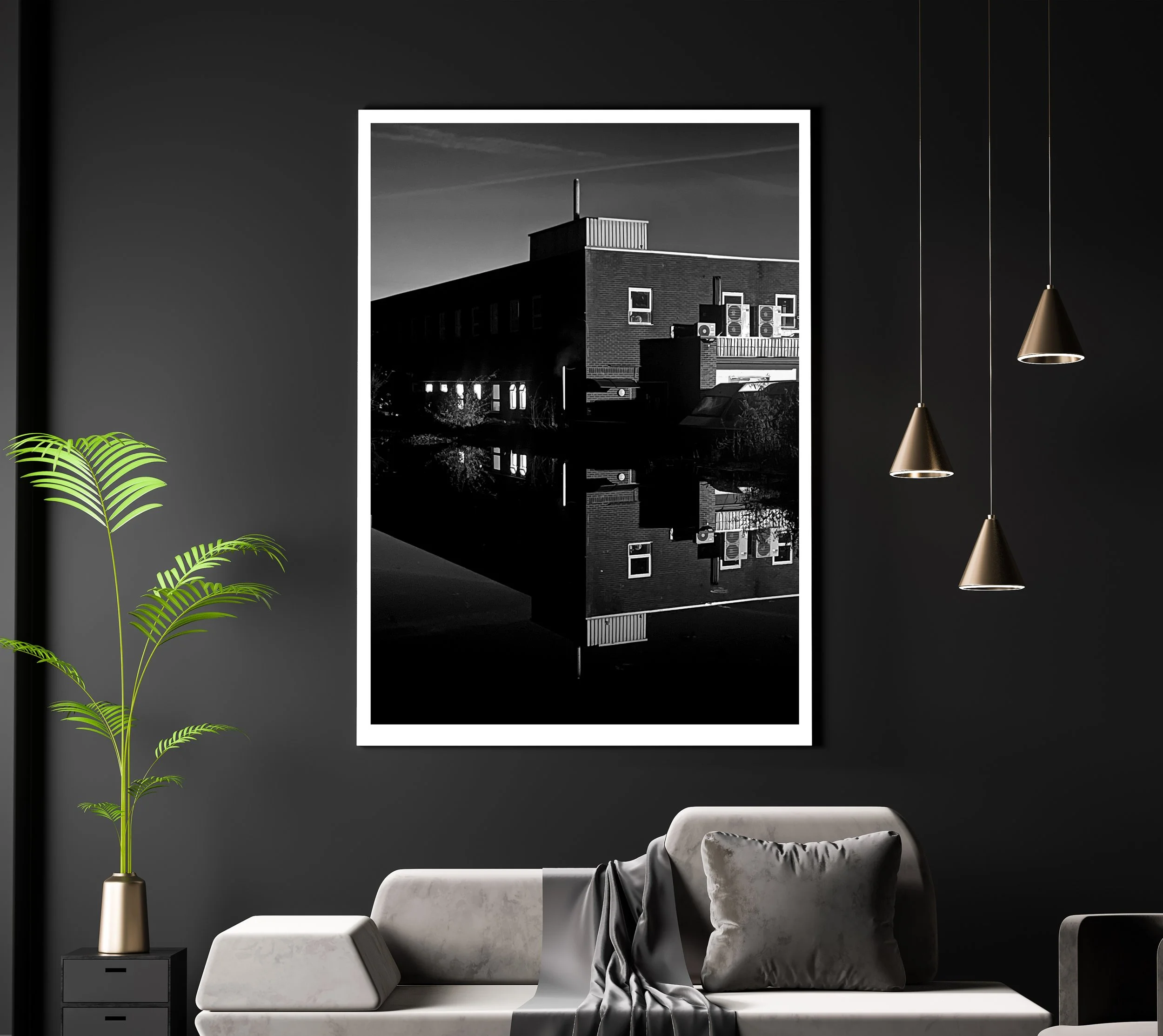 A black and white photograph of a building with a reflection in water, framed with a white border, hanging on a dark gray wall in a modern living room.