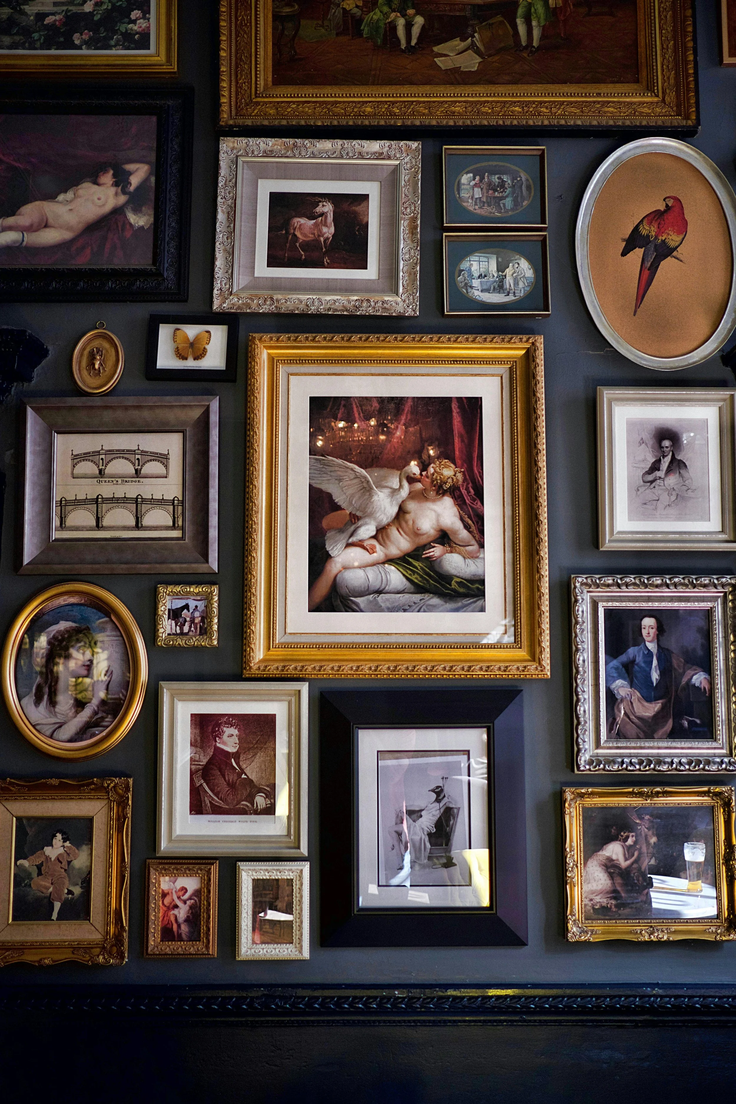 A wall decorated with various framed artworks including paintings, photographs, and drawings, featuring portraits, animals, and abstract images.