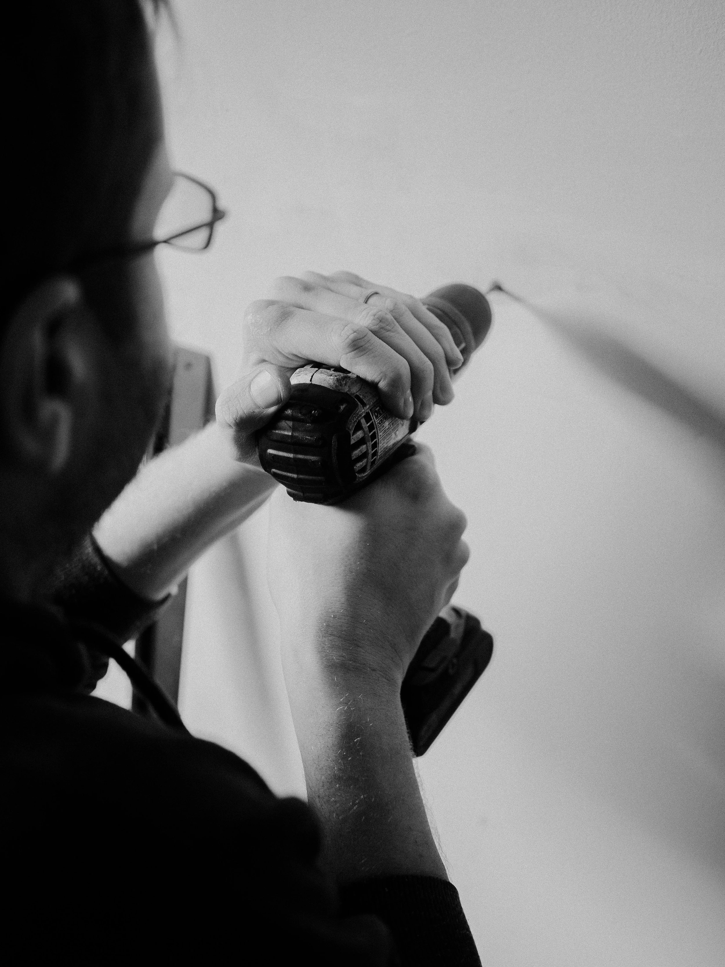 Person holding a cordless drill with both hands, working on a wall or surface.