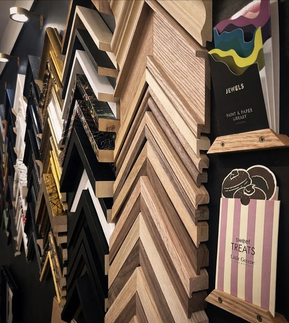 Display of various picture frame samples in different colors, styles, and materials, arranged on a wall for selection.