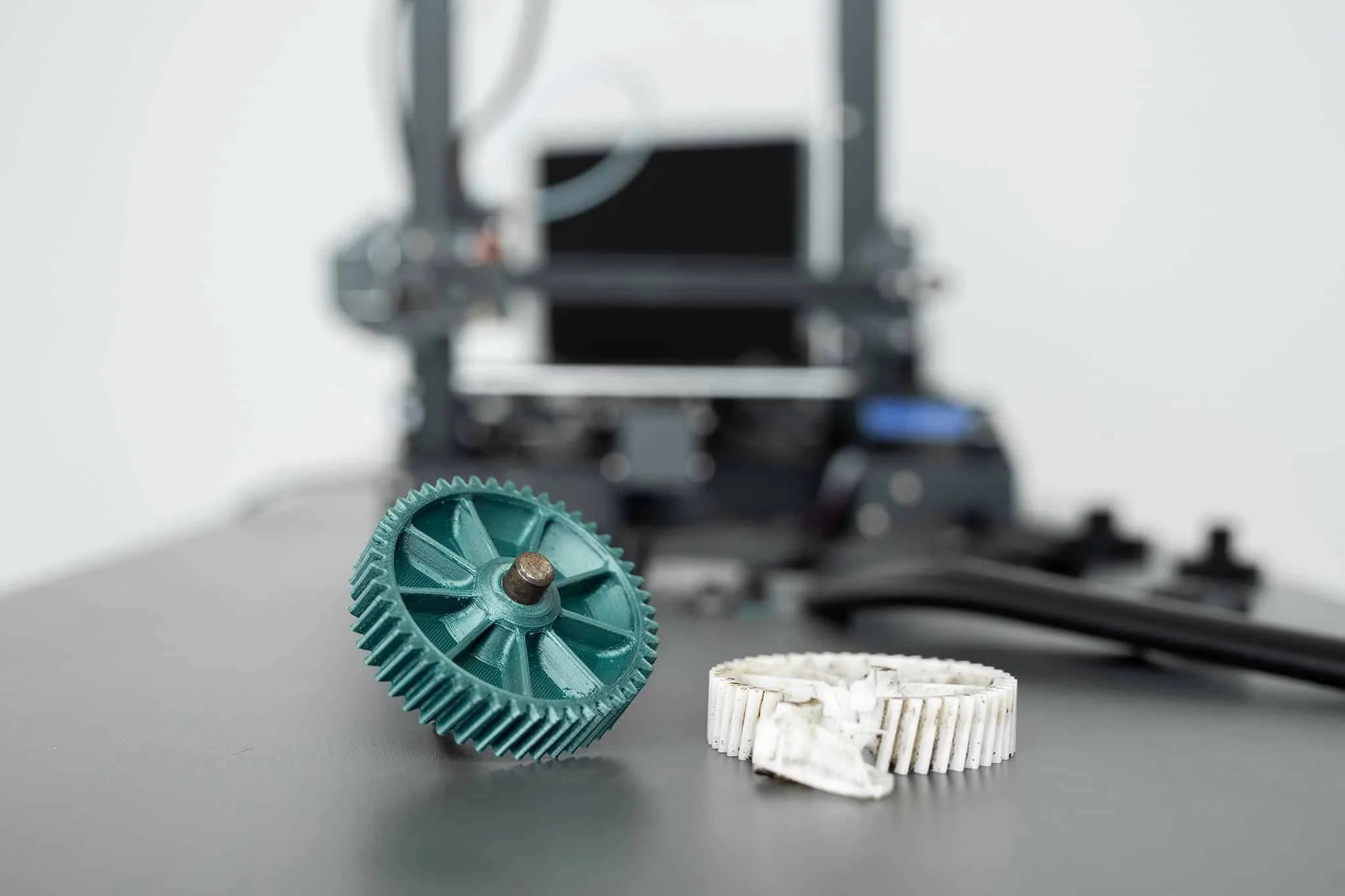 Saplēsts zobrats, kuram blakus atrodas 3D printēts aizvietojums