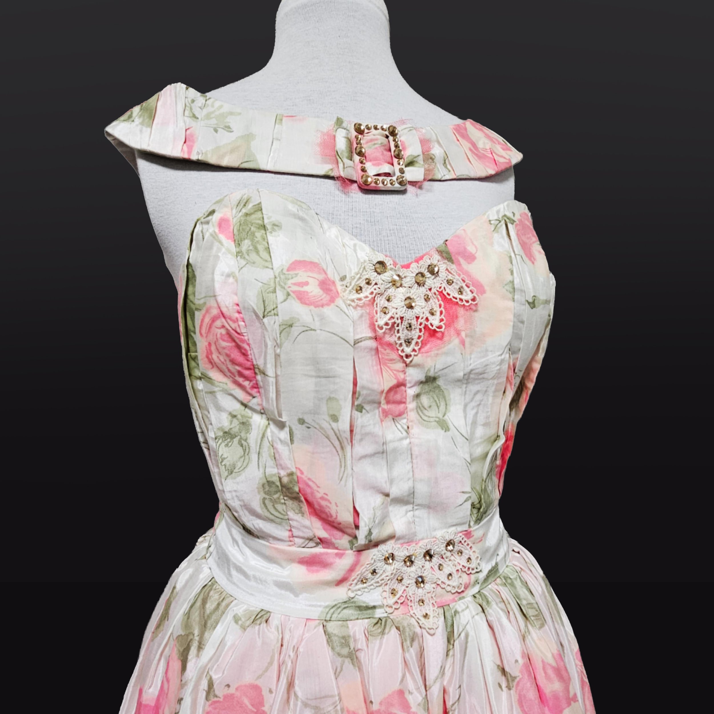 A vintage inspired floral dress on a mannequin, featuring pink and green flowers on a cream background, embellished with lace and gold accents.