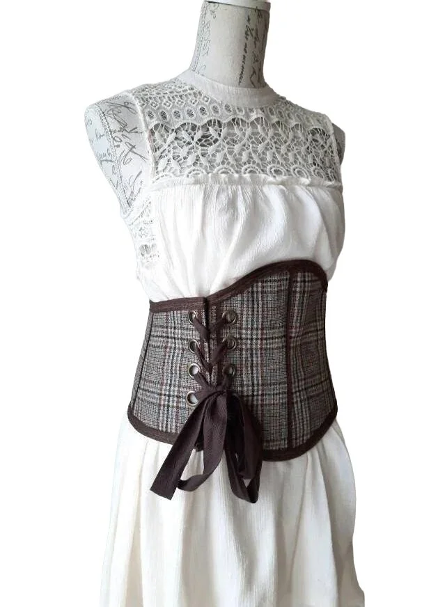 Dress form wearing a white sleeveless top with lace detail and a brown plaid waist corset belt with laced-up front, tied with a dark brown ribbon.