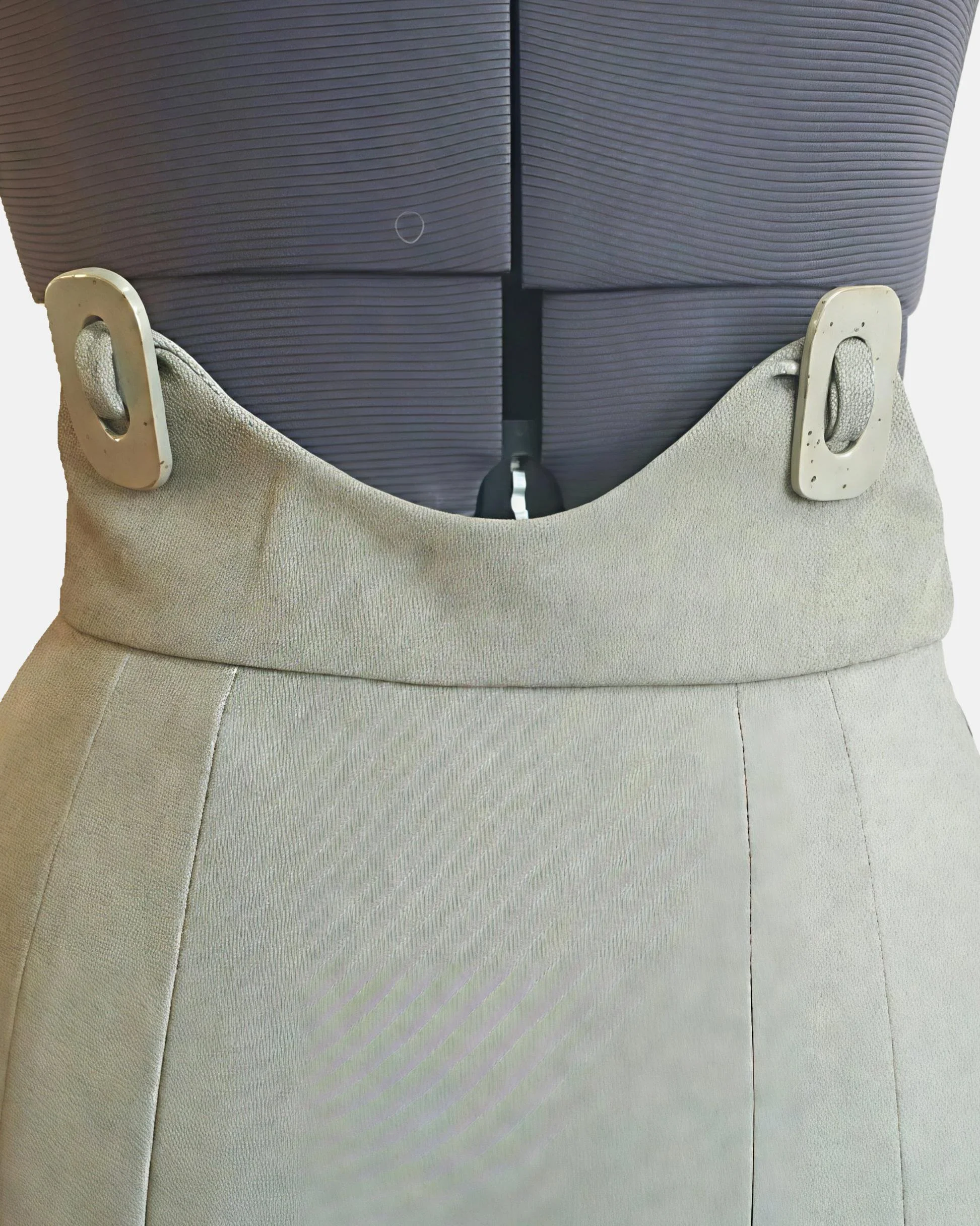 Close up of a beige colored skirt with a high waist, with two large ceramic button accents.