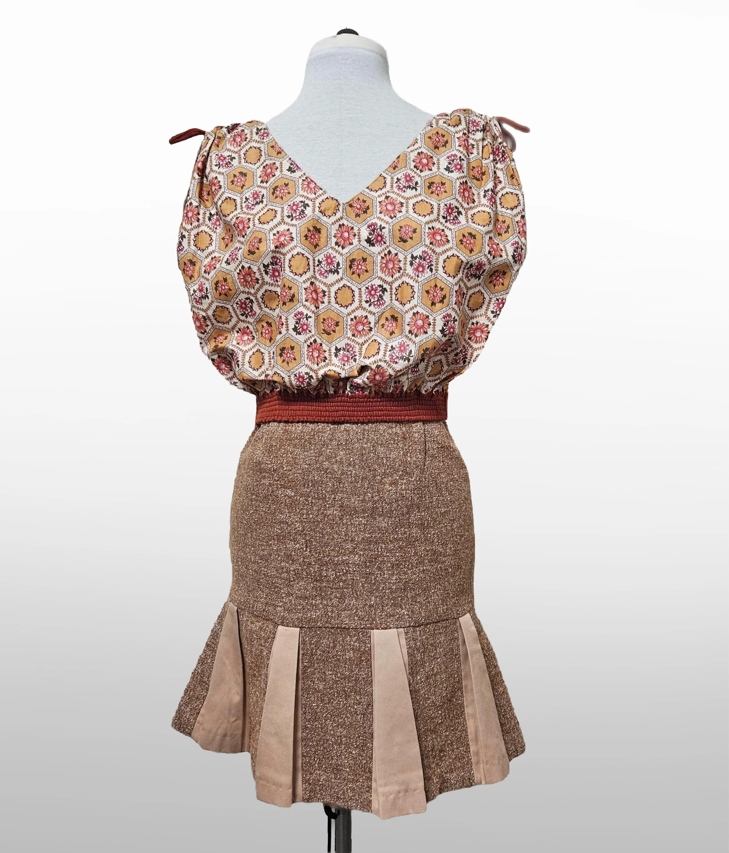 Vintage inspired women's beige and pink outfit on a mannequin, featuring a floral-patterned top with gathered shoulders, and a fit and flare skirt with pleats. 