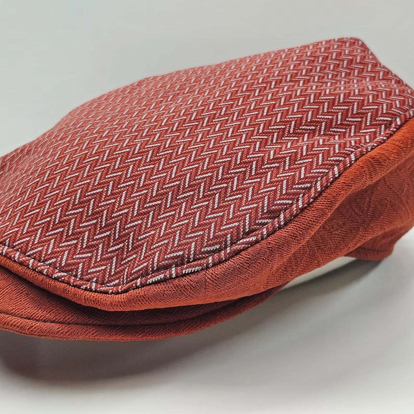Close-up of a red and white patterned fabric flat cap, with detailed stitching and textured material.