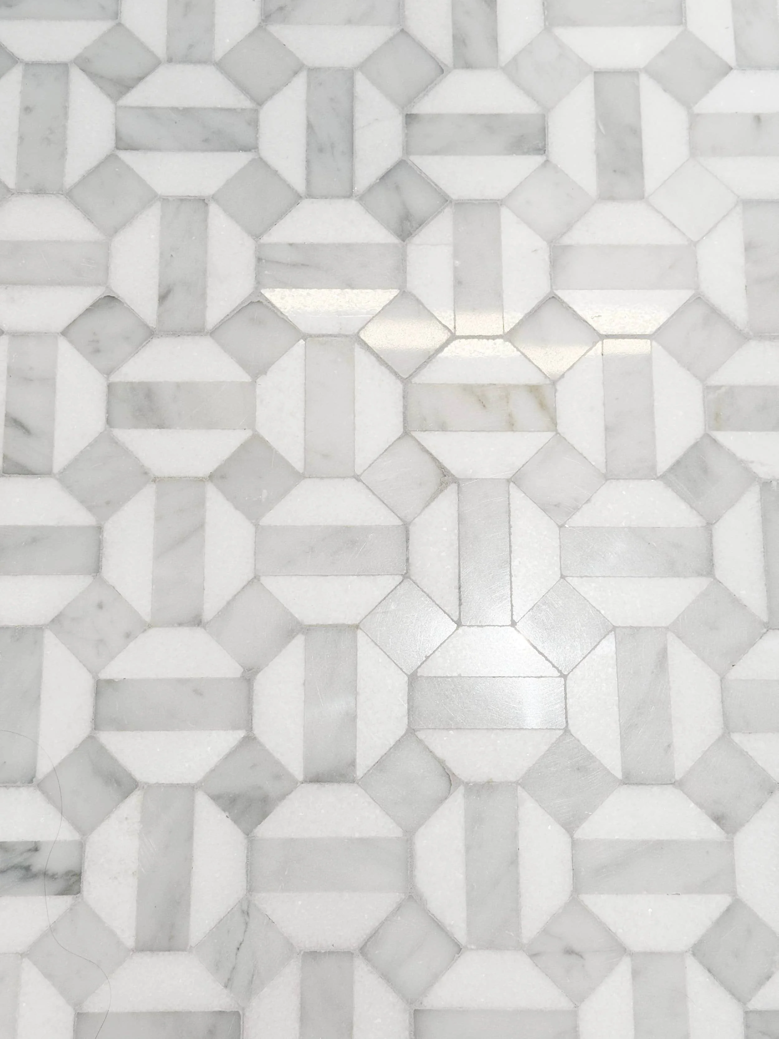 Close-up of a decorative tile floor with geometric pattern in shades of white and gray marble.