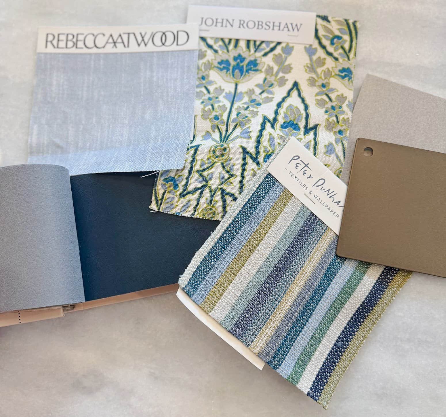 Fabric swatches and color samples for interior design, including patterned and solid textiles with labels from designers Rebeccaatwood, John Robshaw, and Petey Punark.