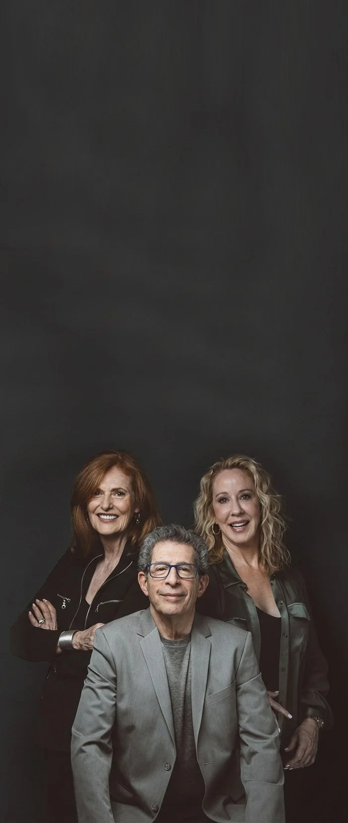 Nancy, Jenell and Mark together, smiling and confident on a dark background and dramatic lighting.