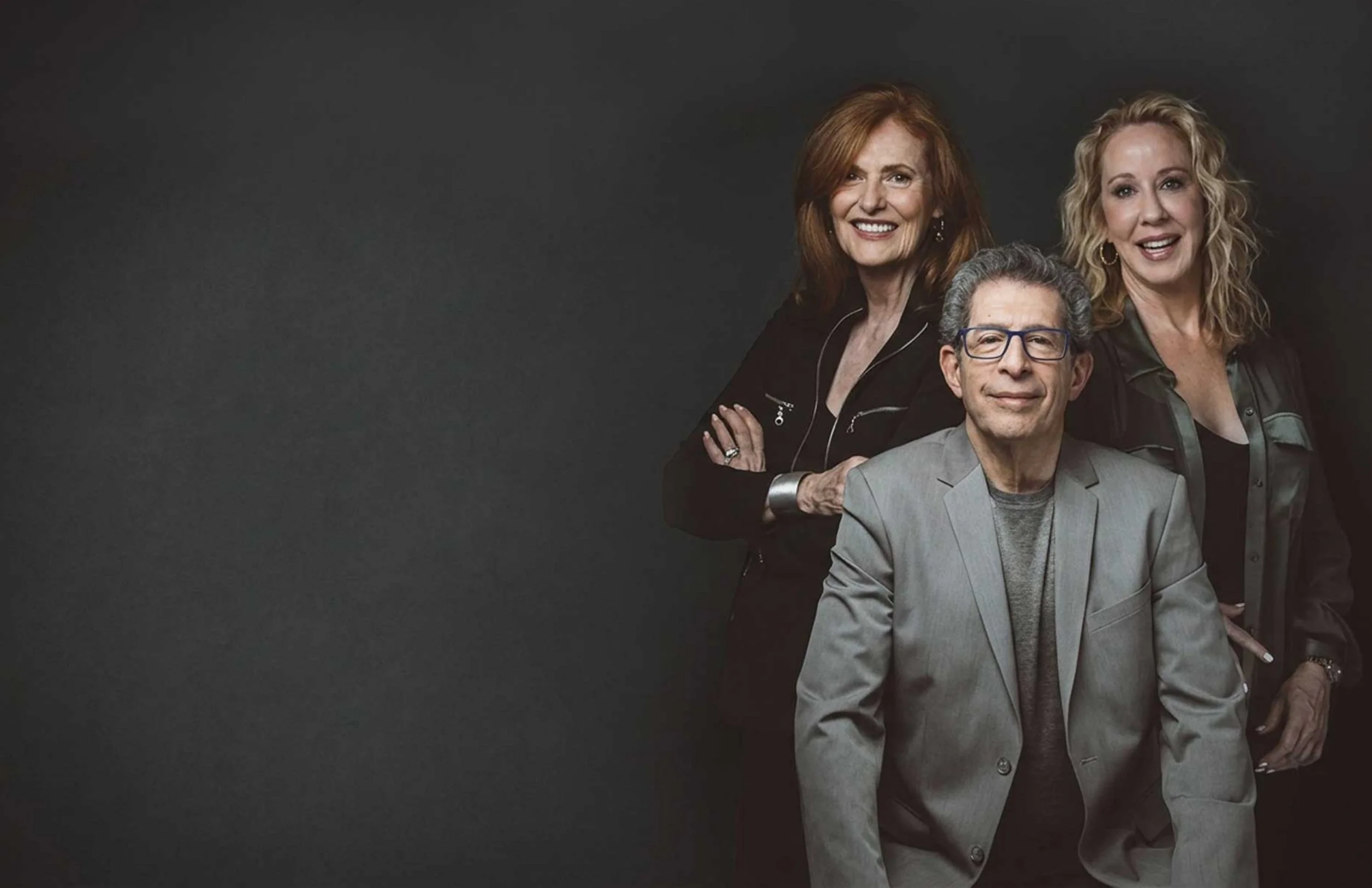 Nancy, Jenell and Mark together, smiling and confident on a dark background and dramatic lighting.