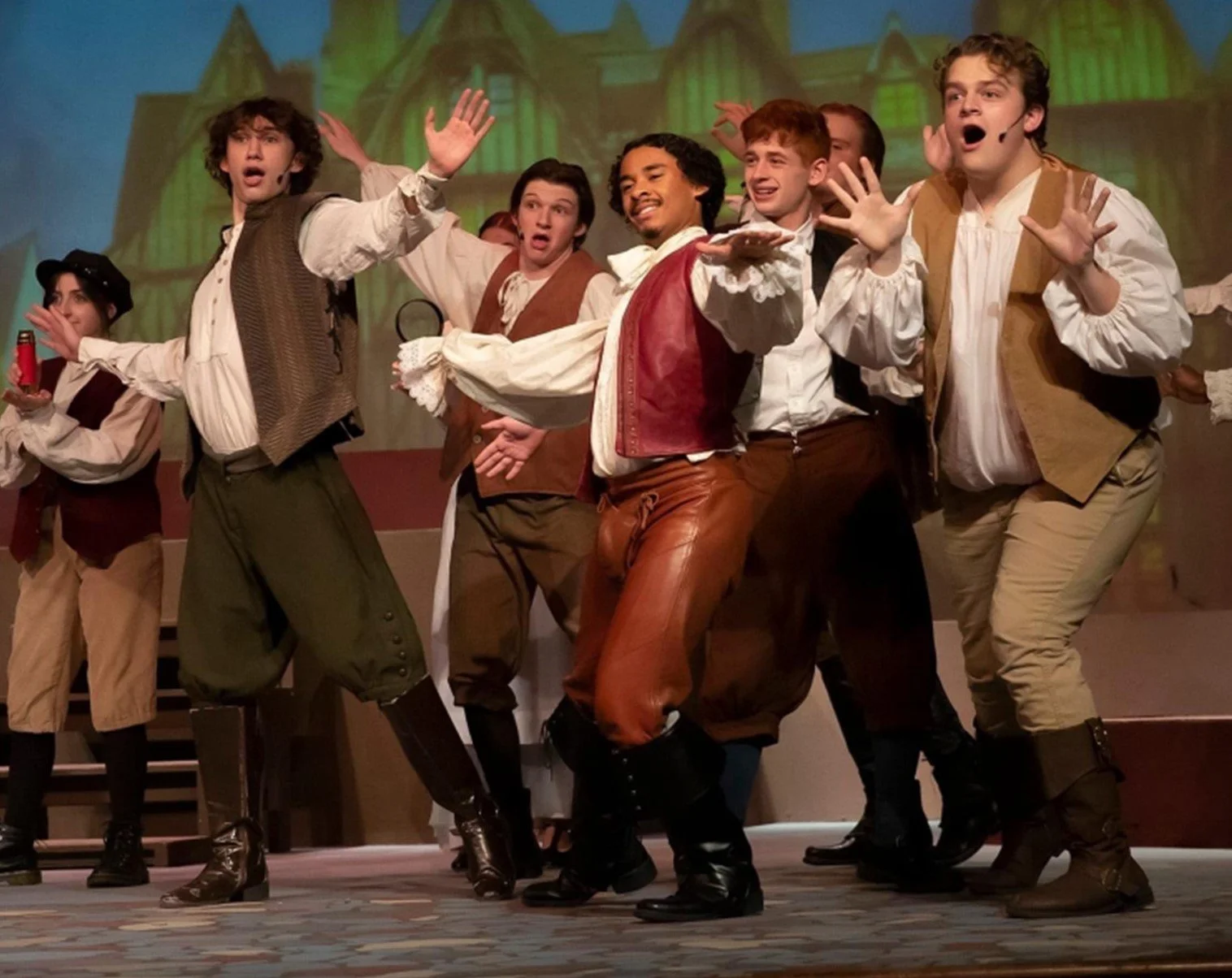 A group of actors on stage performing in 'Something Rotten!' musical, dressed in historical costumes resembling 18th-century European clothing, with a green castle-like set in the background.