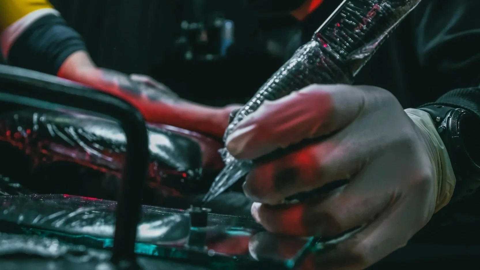 Close-up of a person wearing gloves, holding a pen, and working on electronic hardware with various circuit boards and components.