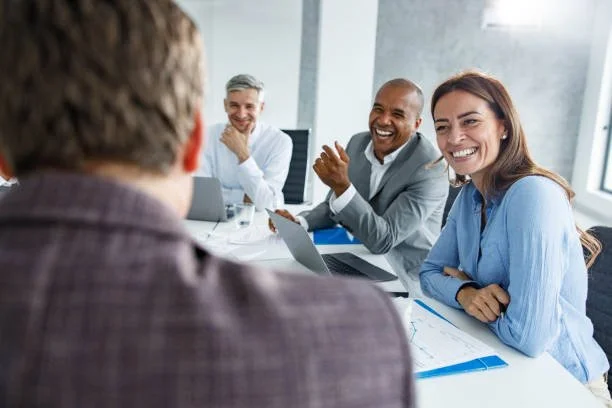 A group of four diverse professionals sitting around a conference table, smiling, in a modern office setting.