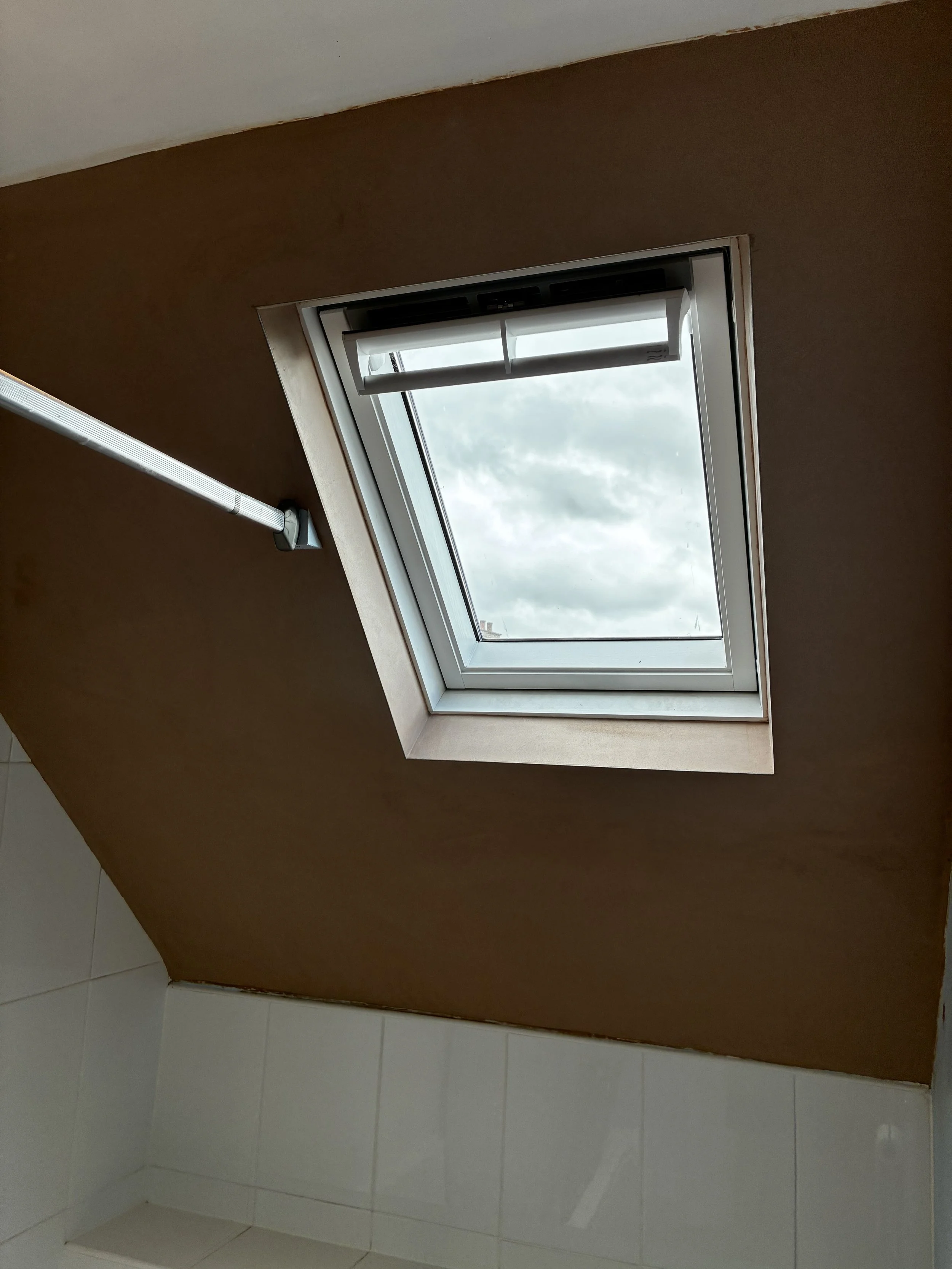 Ceiling opening with a window showing cloudy sky, brown and white walls, and tiled floor.