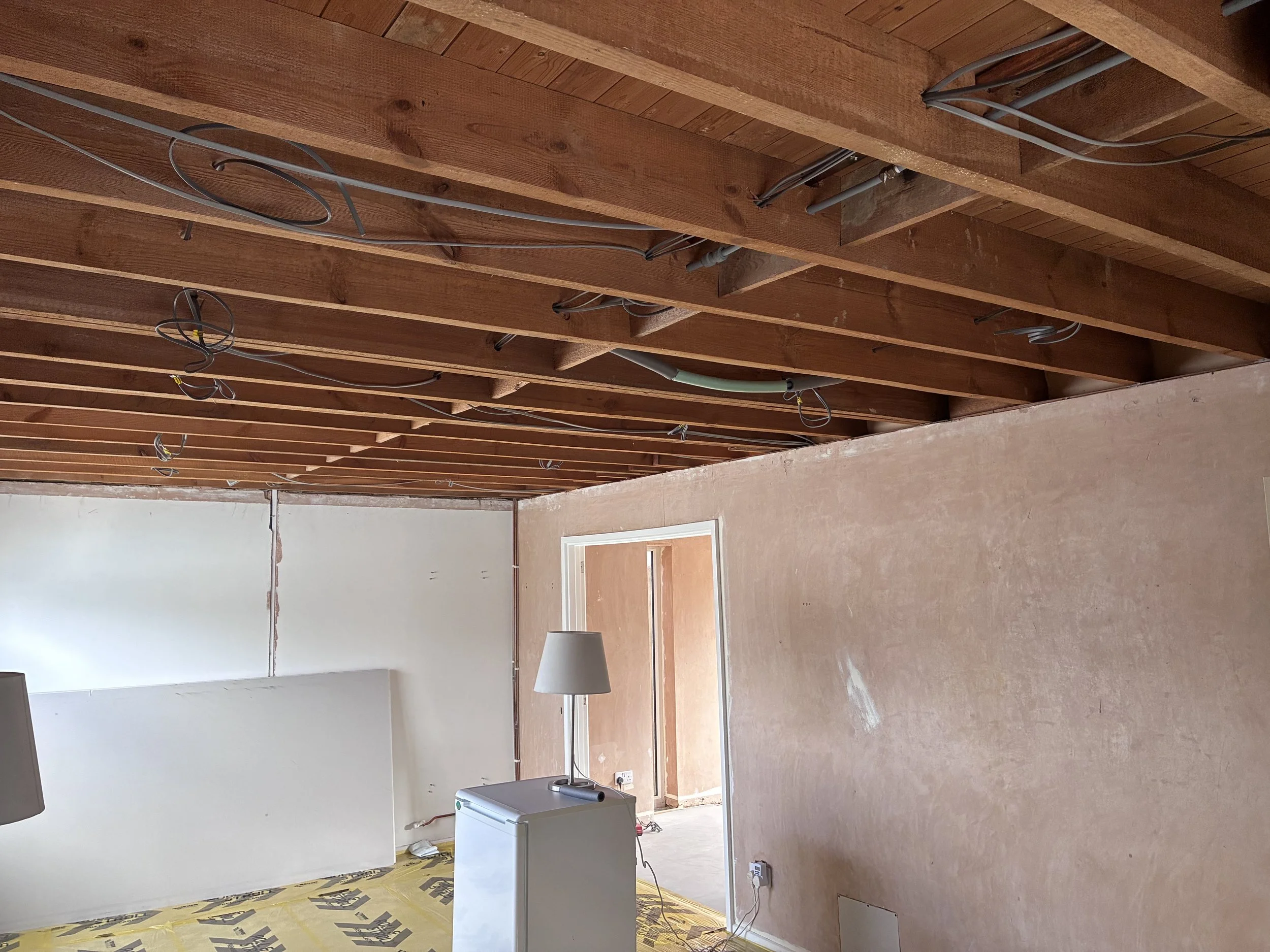 Lounge undergoing plastering preparation with existing walls and exposed ceiling joists before plasterboard installation