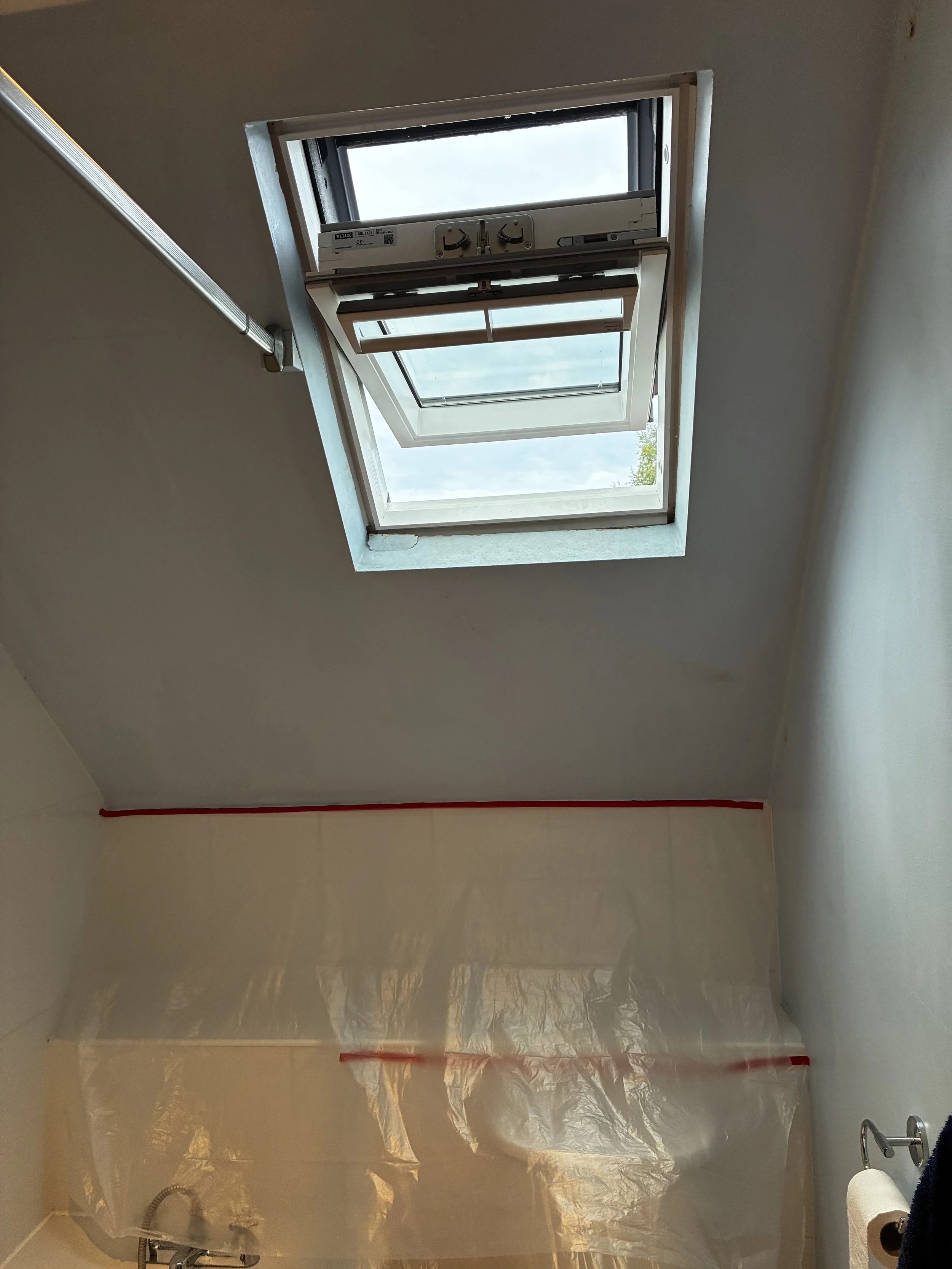View of a bathroom ceiling with an open skylight window, plastic sheeting covering the walls below, and a towel or cloth hanging on a hook next to the sink.