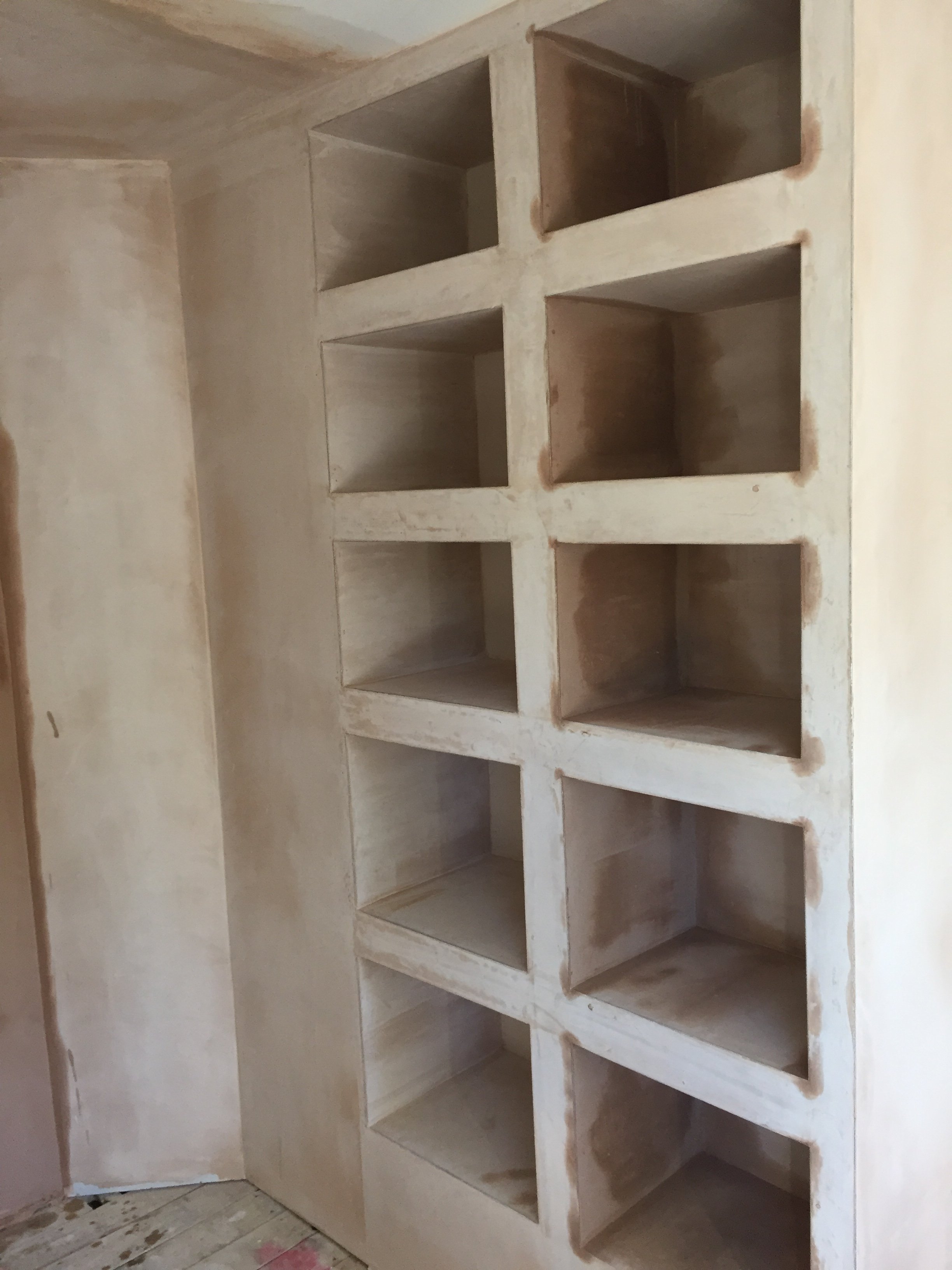 Unfinished built-in shelving unit with multiple square cubbies, in a room under construction.