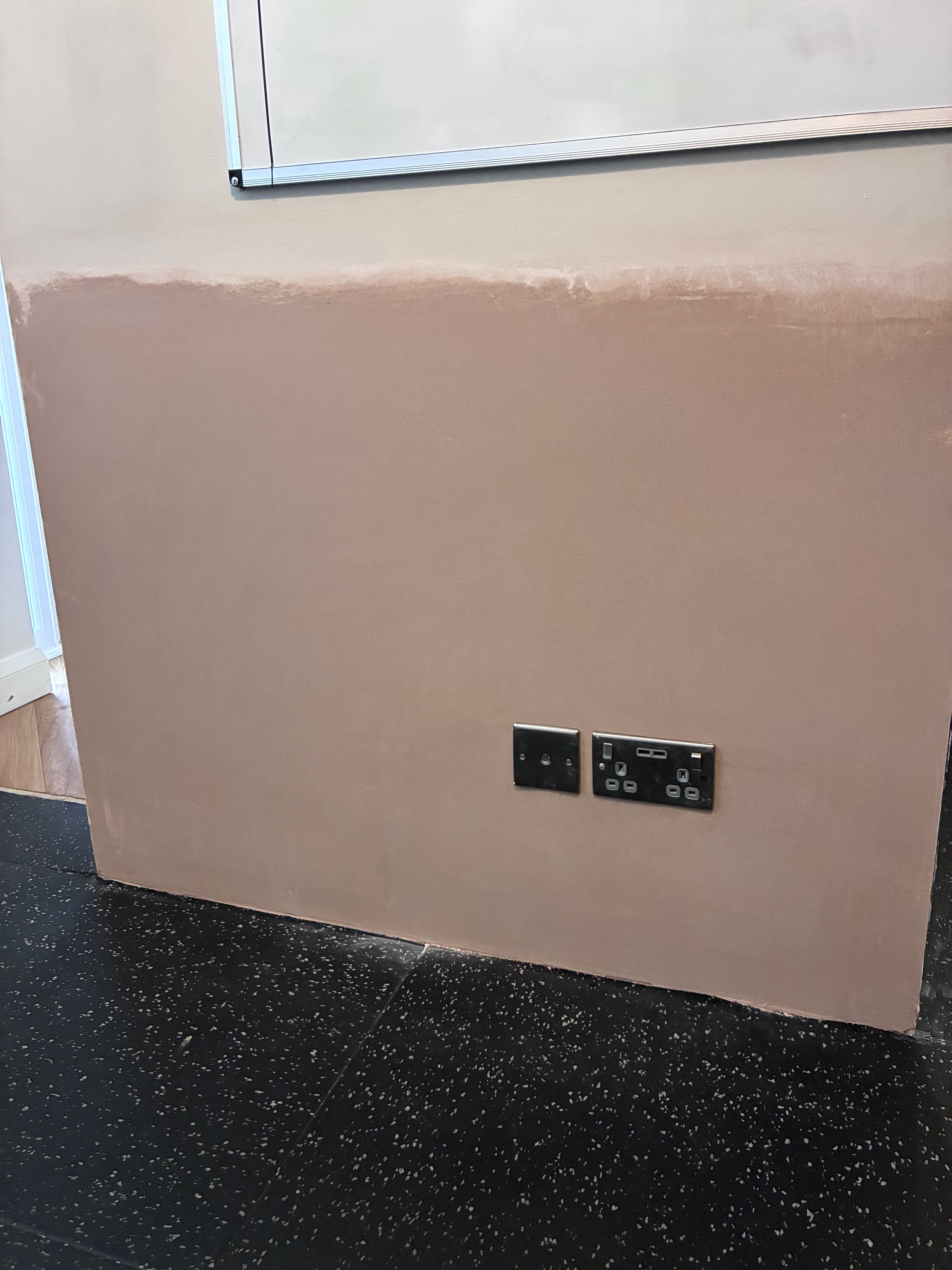 Interior wall with electrical outlets and a whiteboard, in a room with black speckled flooring.