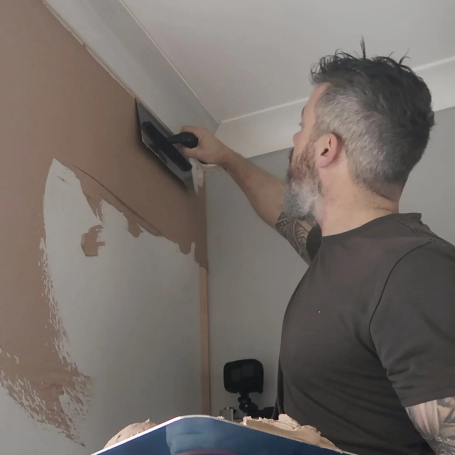 A man with a beard and tattoos painting a wall with a squeegee.