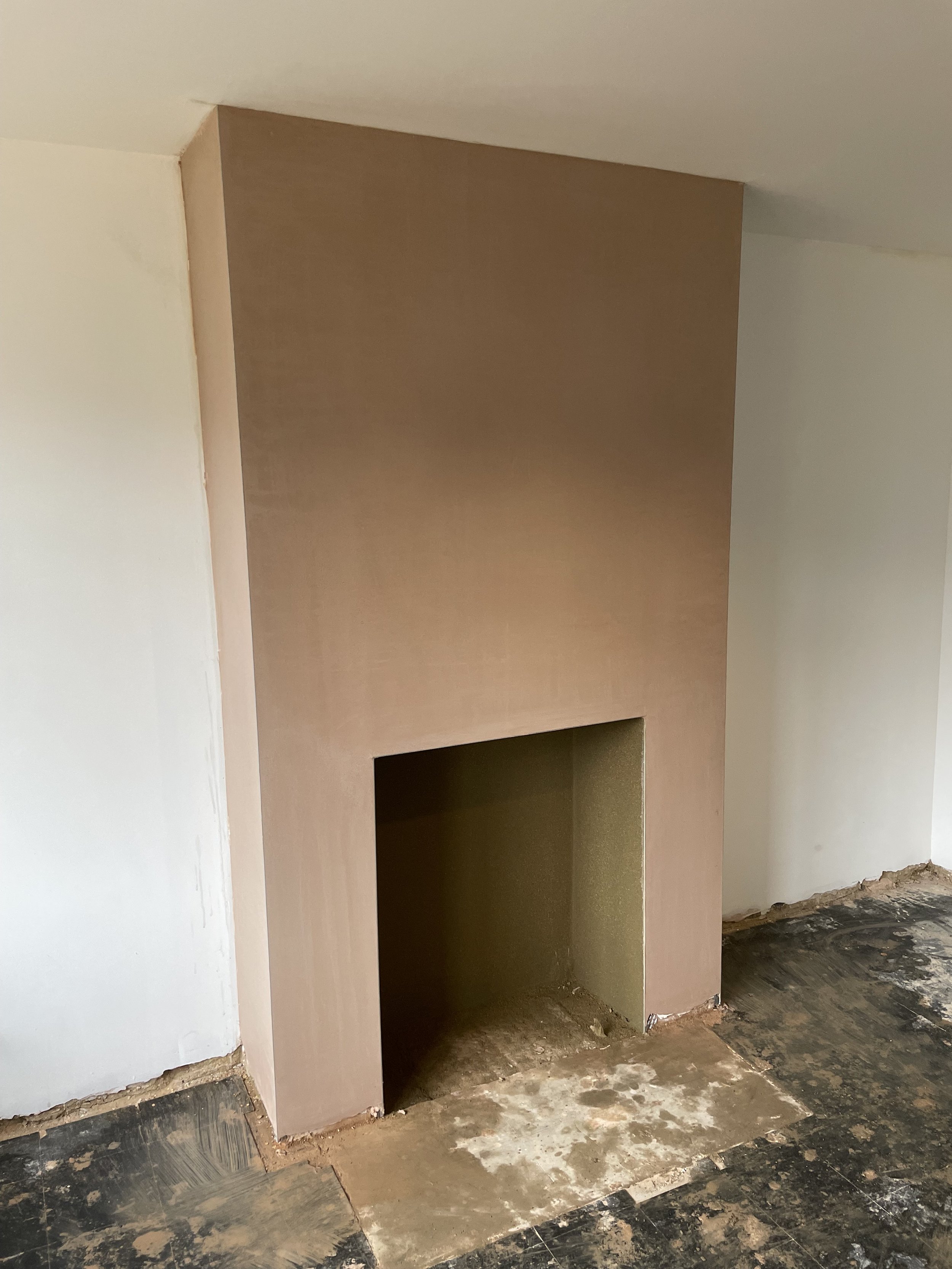 A partially built or renovated fireplace with a beige surround and blackened, unfinished wooden flooring