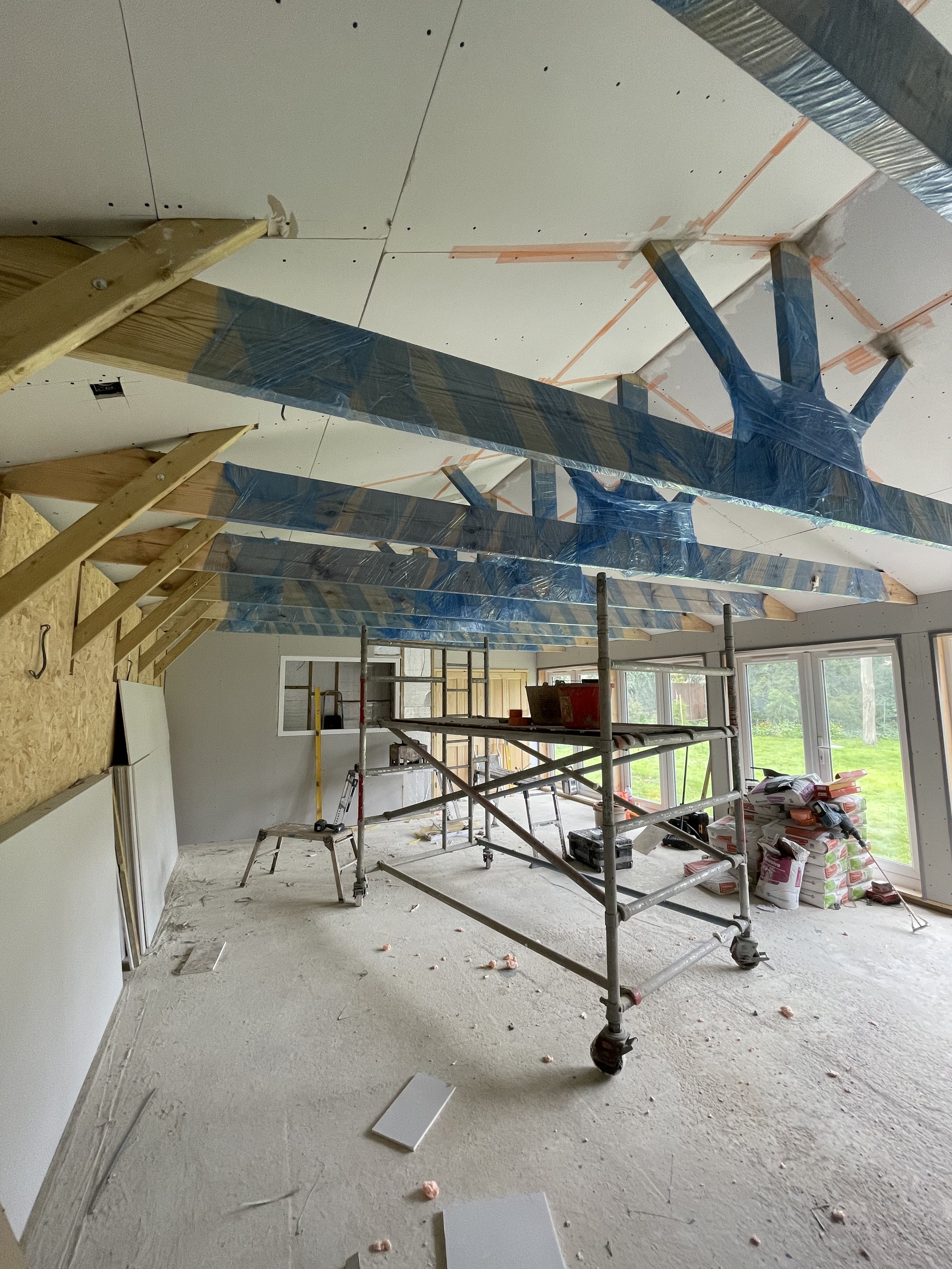 Interior of a room under construction with scaffolding, insulation, and drywall being installed on the ceiling.