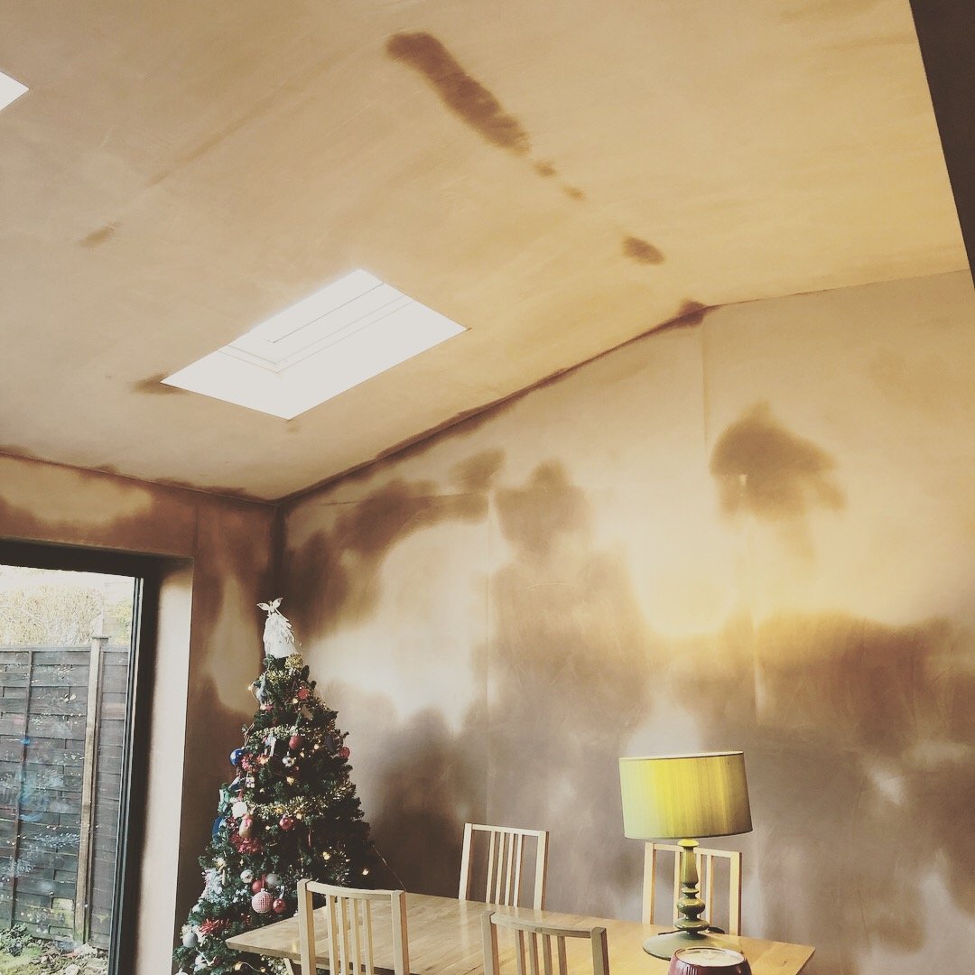 Room with a Christmas tree, a wooden table, chairs, and a yellow lampshade; the walls and ceiling are stained or discolored.