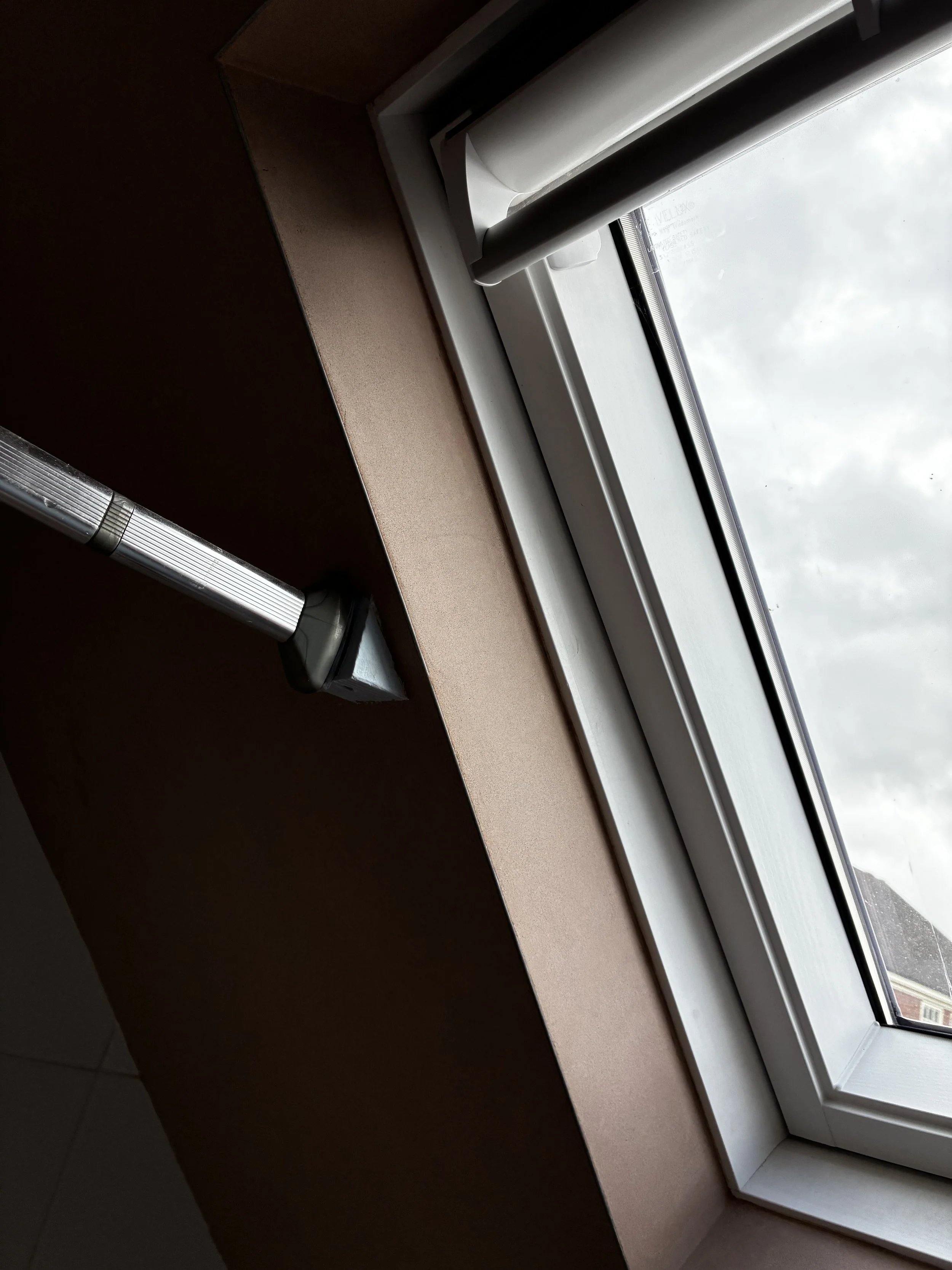 Close-up of a window with an open white window blind, looking outside at an overcast sky.