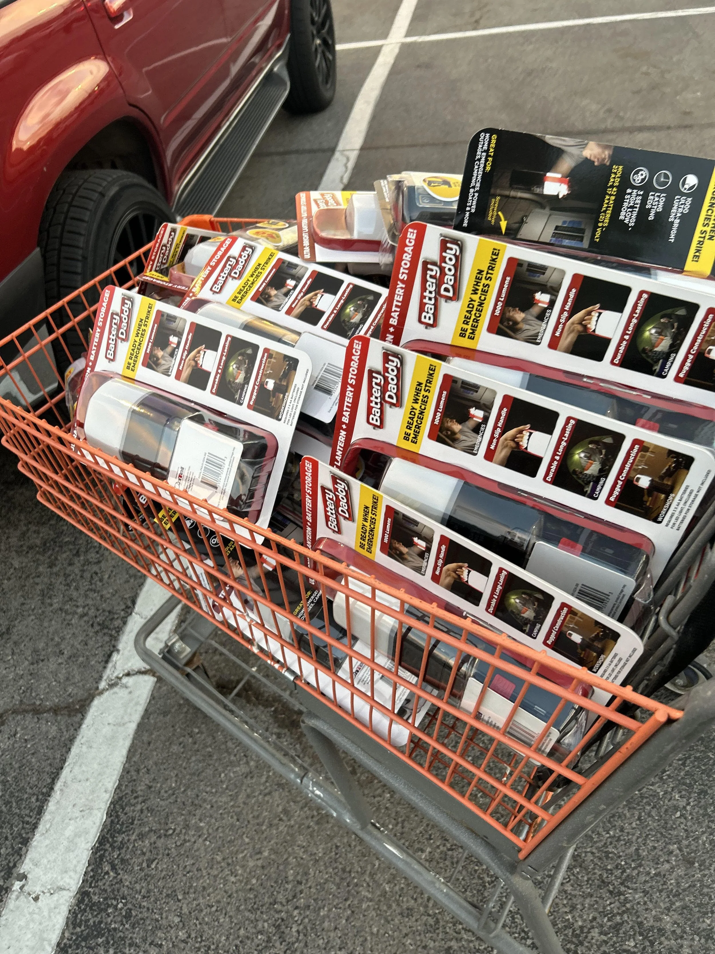 Shopping cart filled with safety emergency flashlight, placed in a parking lot next to a red vehicle.