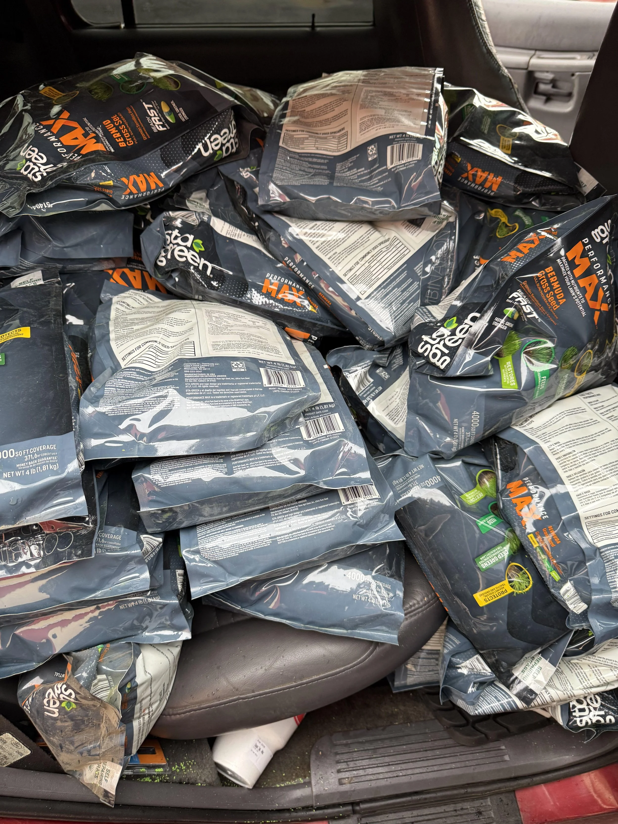 Multiple bags of Stealgreen MAX performance dog food stacked on car seat and floor.