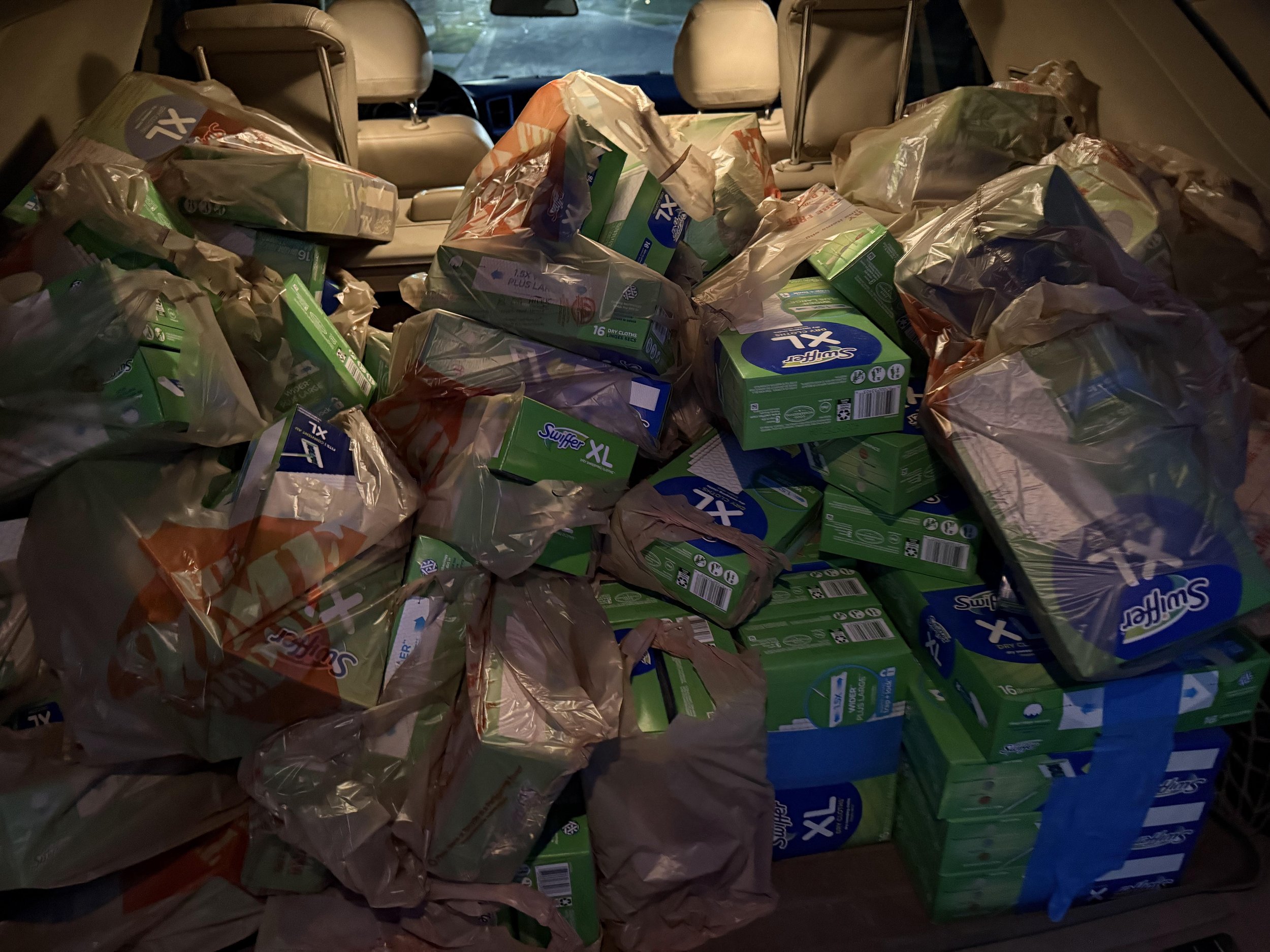 Back of a vehicle loaded with multiple bags of paper towels and tissue boxes.