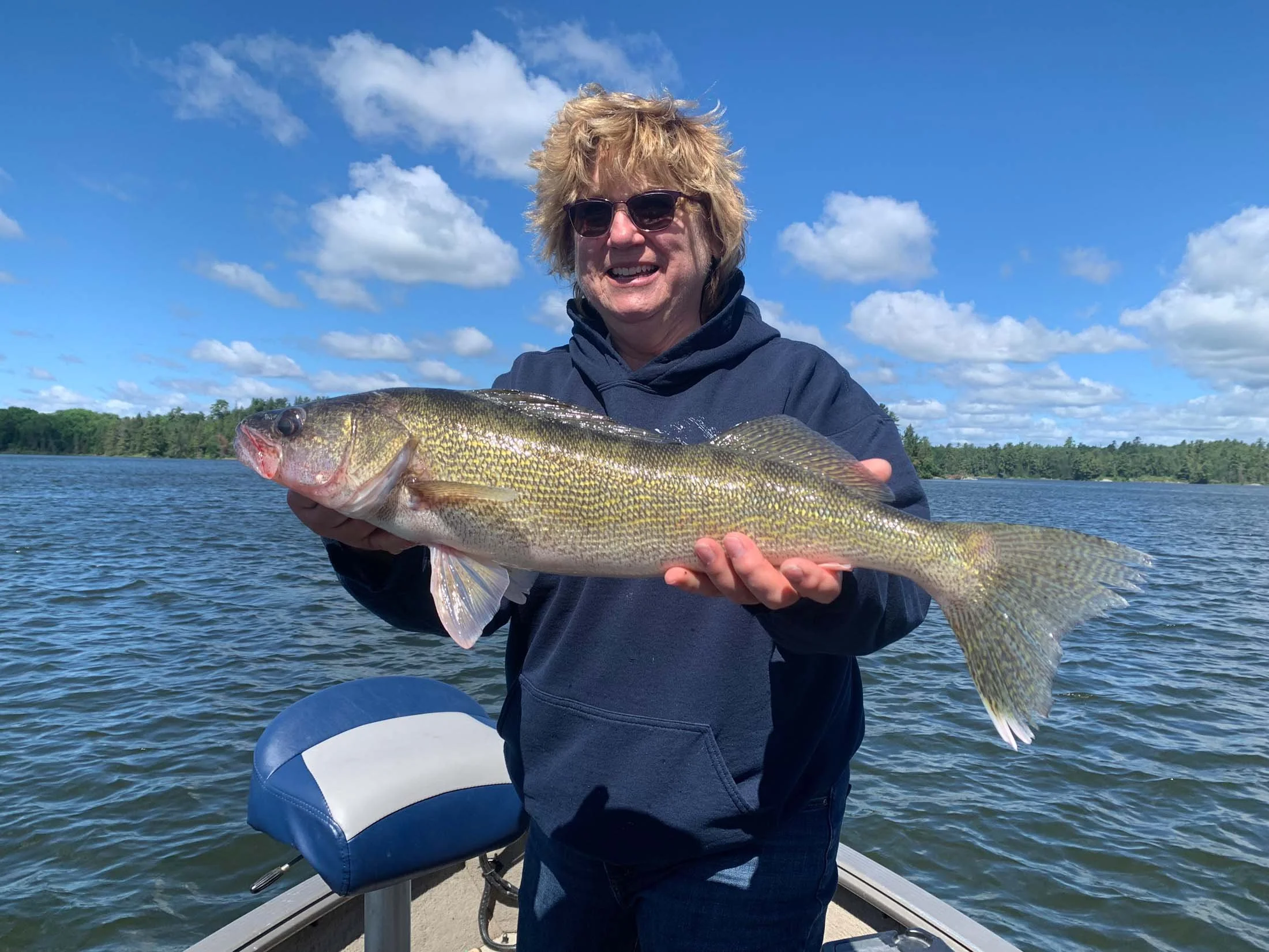 Person outdoors on a boat holding a large fish, with blue sky and white clouds in the background.