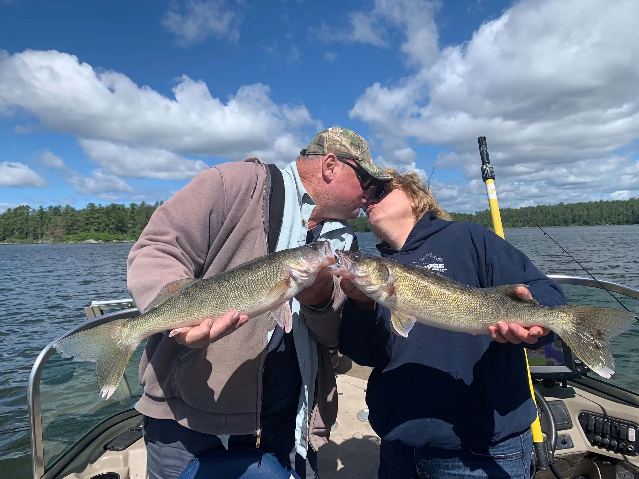 Two men are on a boat holding up a large fish they caught, with clouds and water in the background.