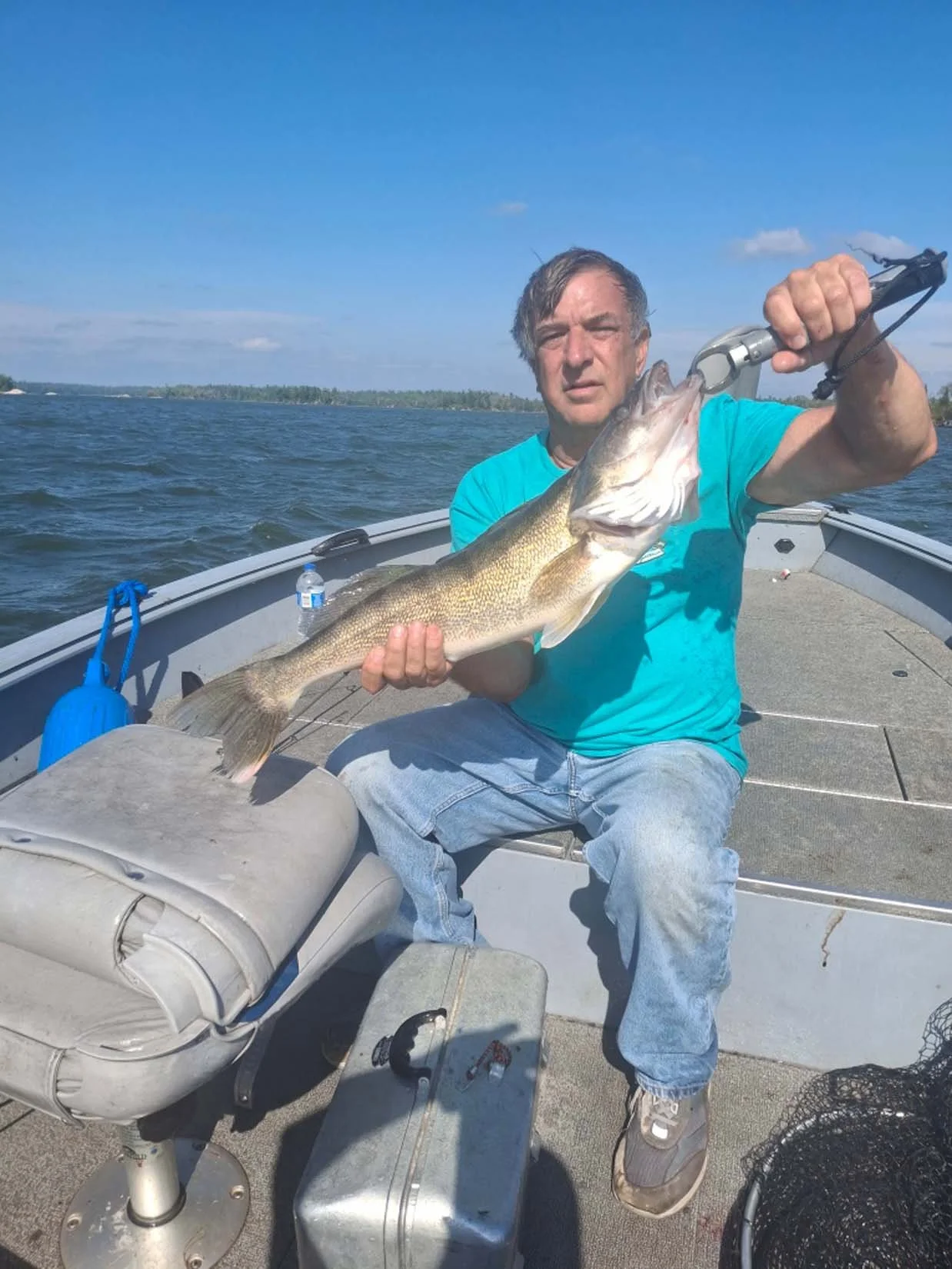 A man sitting in a boat holding a large fish he just caught while fishing on a lake.