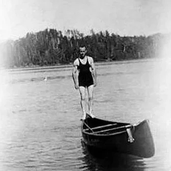 Person standing on a small boat on a body of water with trees in the background.