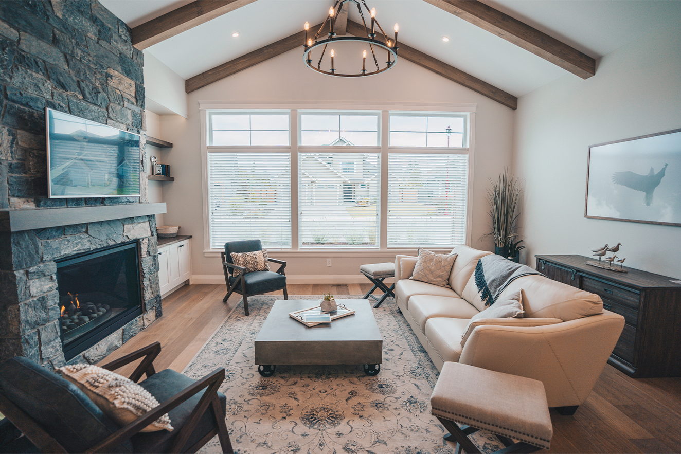 Gemütliches Wohnzimmer mit Kamin, großem Fenster, weißen Sofa, schwarzen und Holzgartenstühlen, Holzboden, moderner Deckenleuchte, Wandkunst eines Vogels, Dekofiguren von Vögeln auf Kommode, Pflanzen und Kissen.