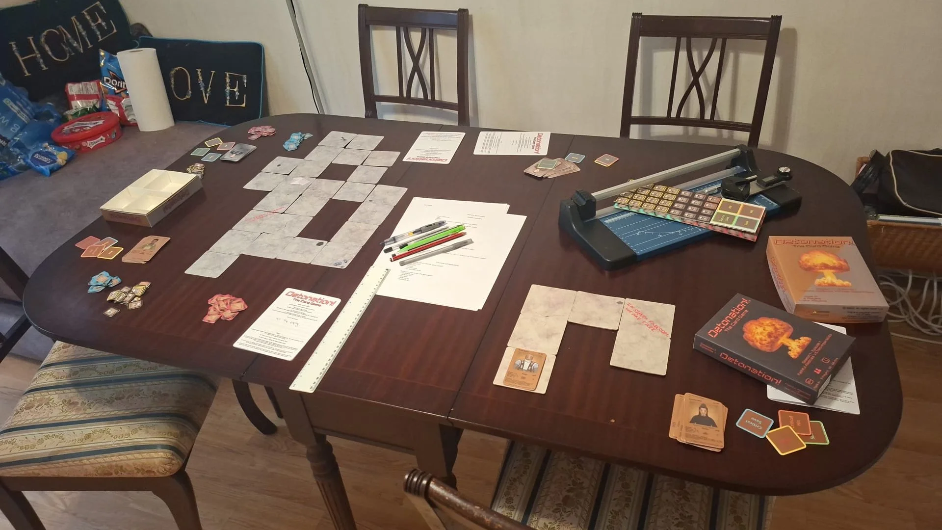 Setting up prior to People playing the card game 'Detonation! The Card Game' December 2025. a table with game pieces, cards, and instruction sheets.